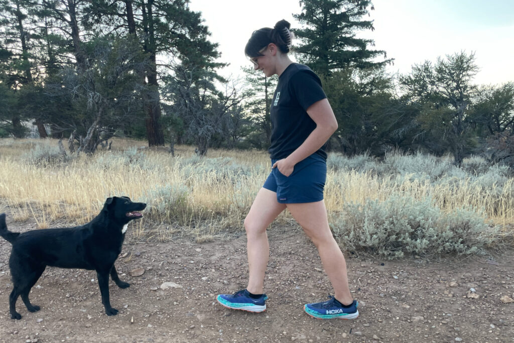 a women hiking on a dirt road with a black dog in the patagonia multi-trails shorts