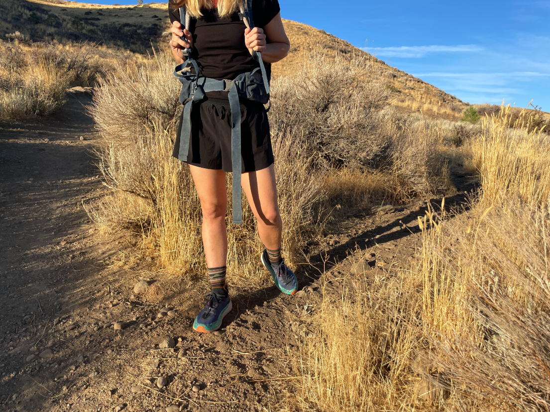 a backpacker on a desert trail at golden hour under a bright blue sky wearing black janji shorts