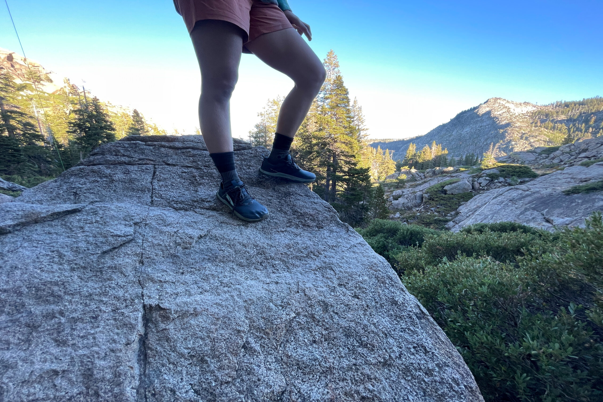 a hikers on top of a large granite boulder in the shade wearing altra lone peak 8 hiking shoes