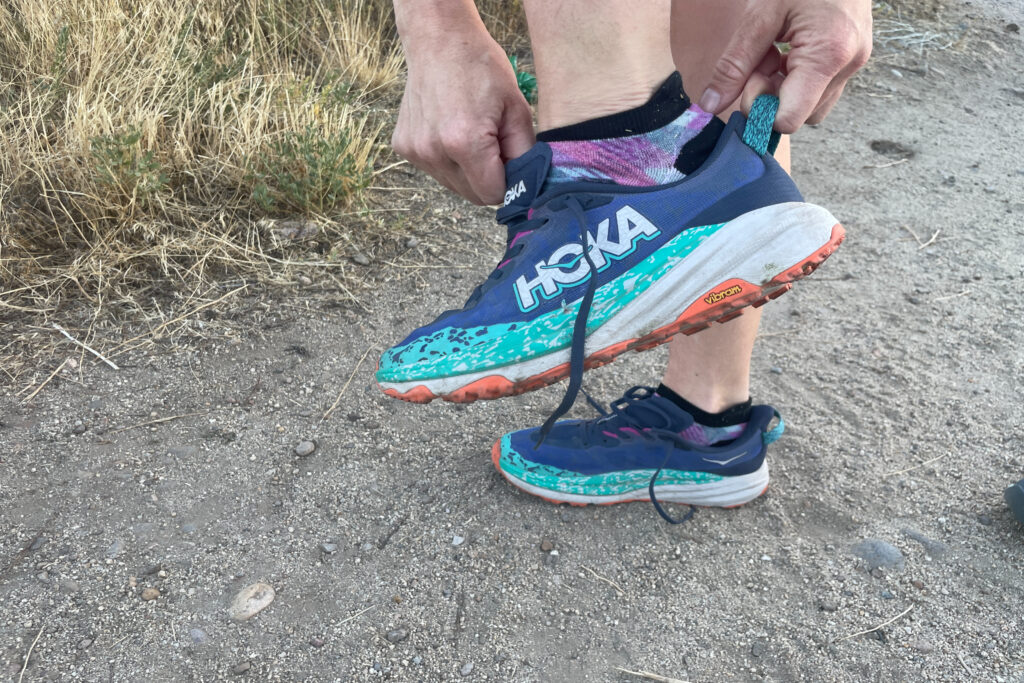 a hiker pulling on the hoka speedgoat 6 onto their foot with the tongue and heel loop