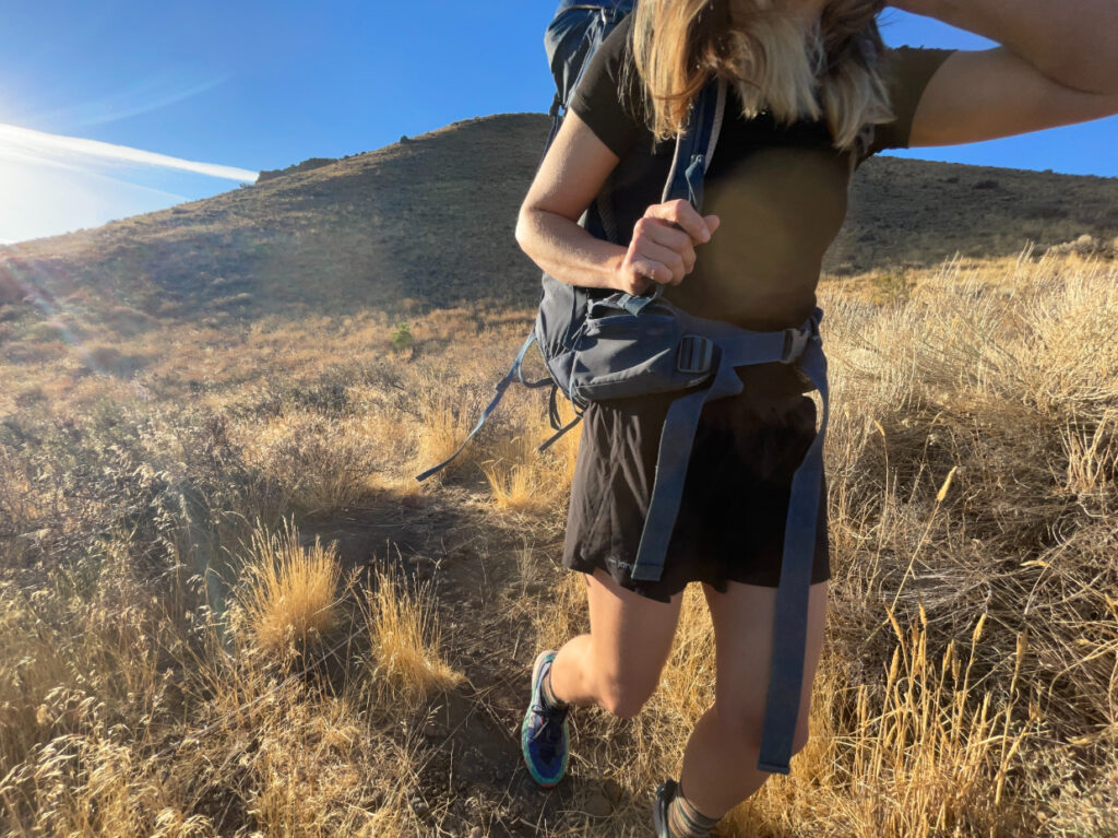 a backpacker hiking in a desert meadow with w butte in the background