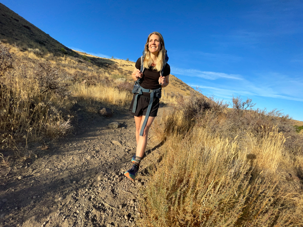 a hiker under a bright blue sky walking on a sandy desert trail