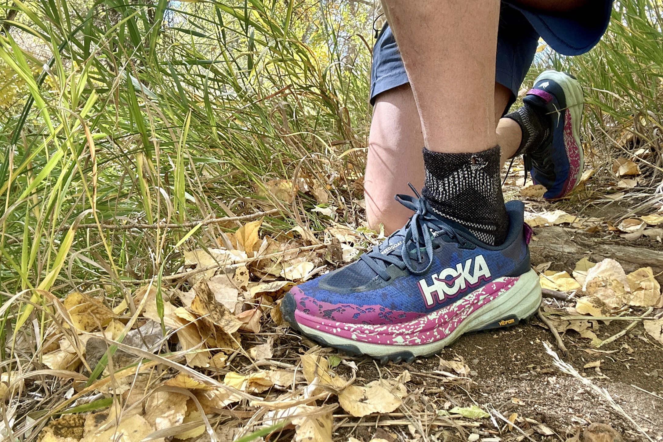 Close up of a pair of shoes with a man bending down on a trail.