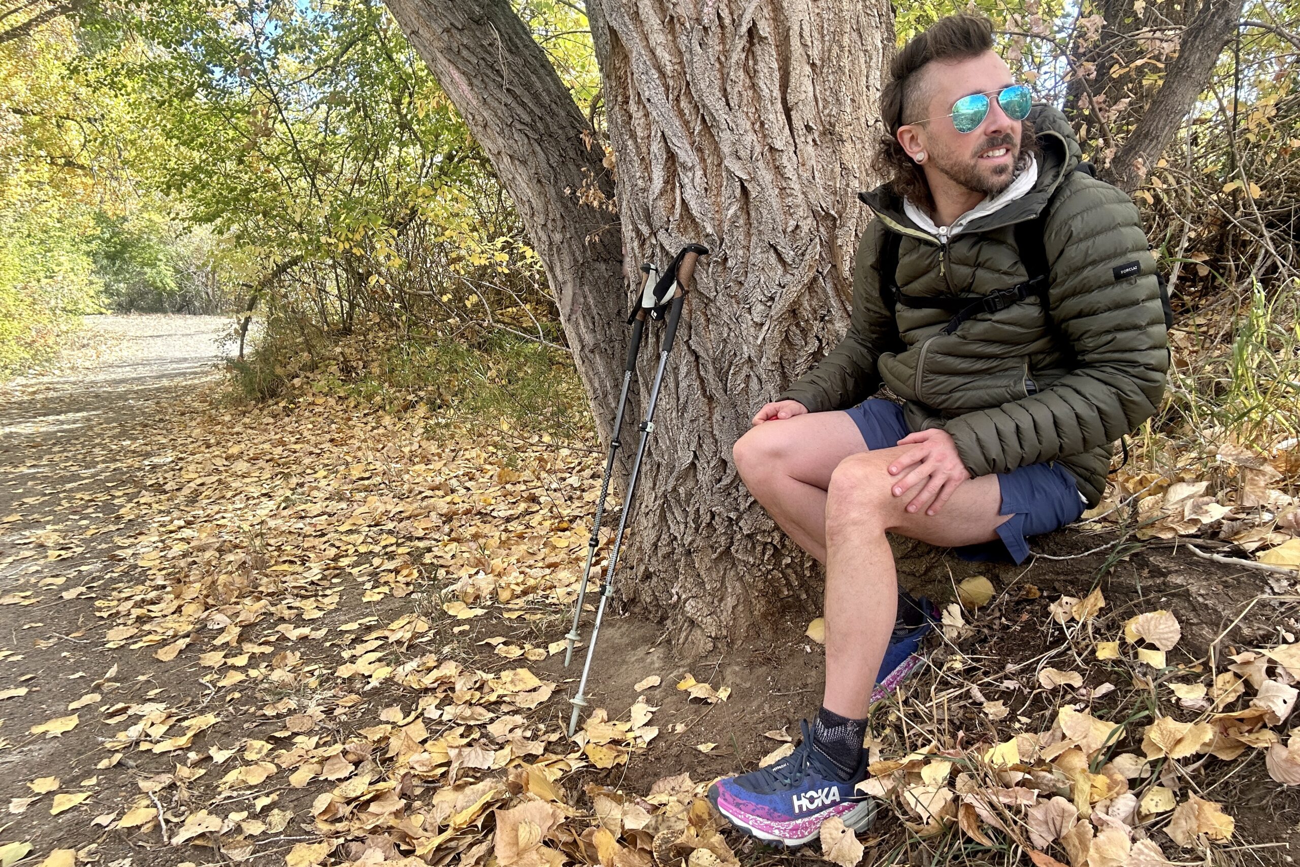 A man looks off in the distance, sitting on a tree root, after tying his shoes.