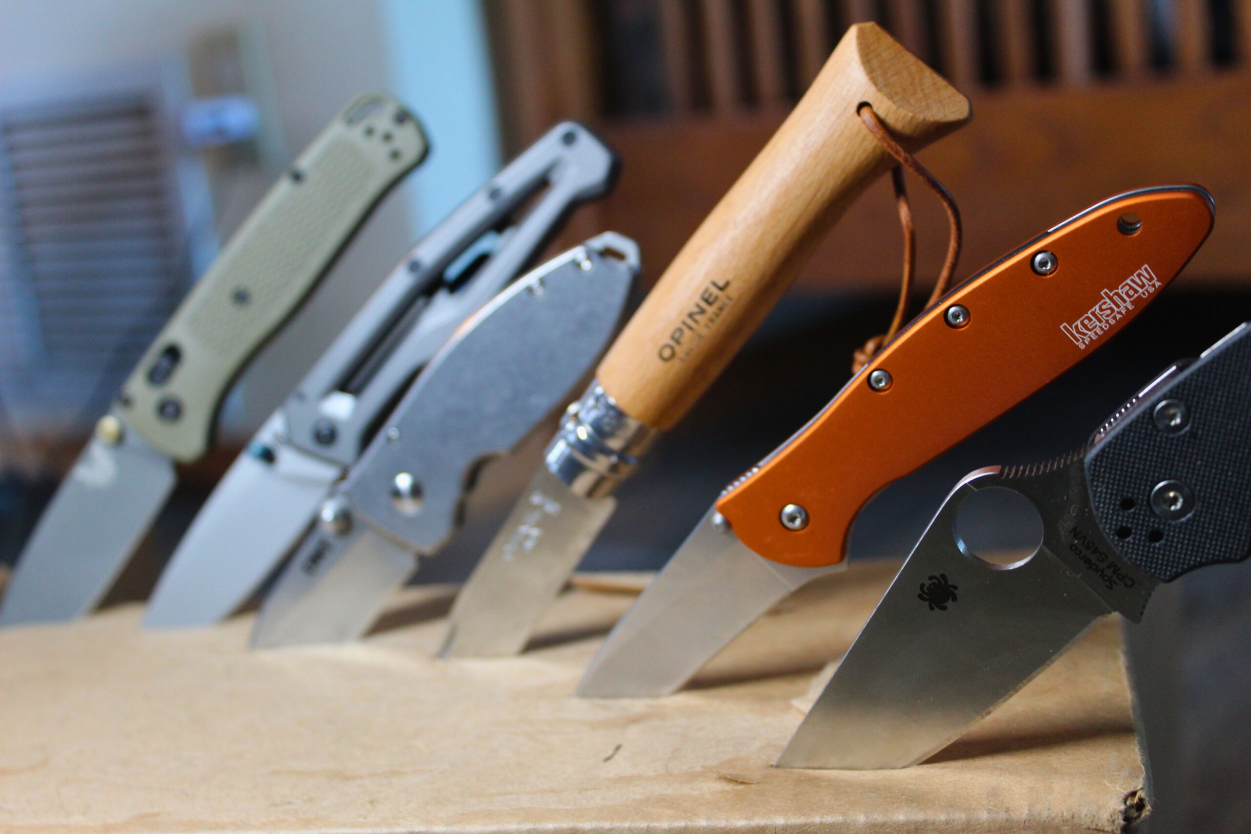 A grouping of knives with blade tip stuck into cardboard.