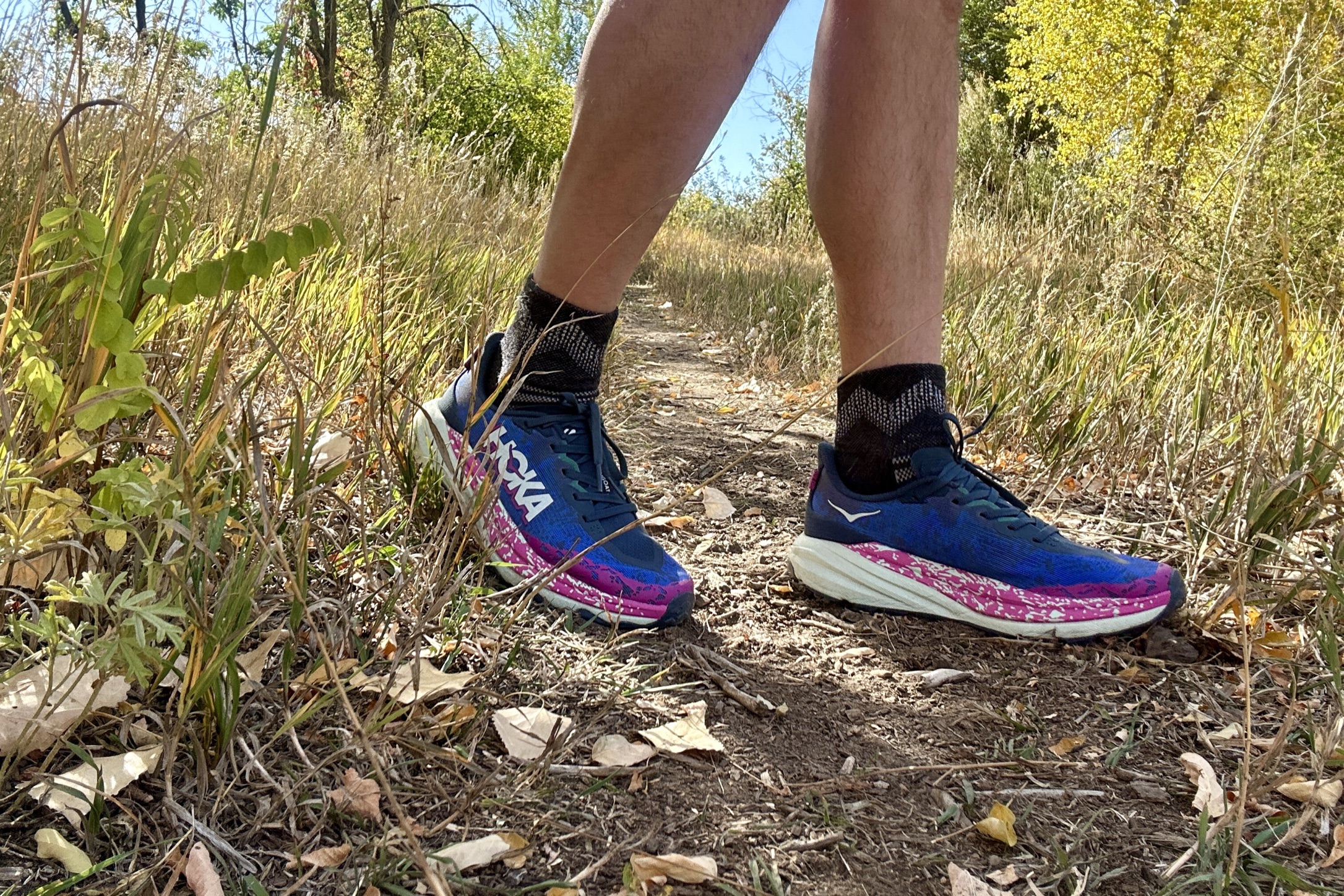 Close up of a man from the knees down walking on a trail with shoes in the center.