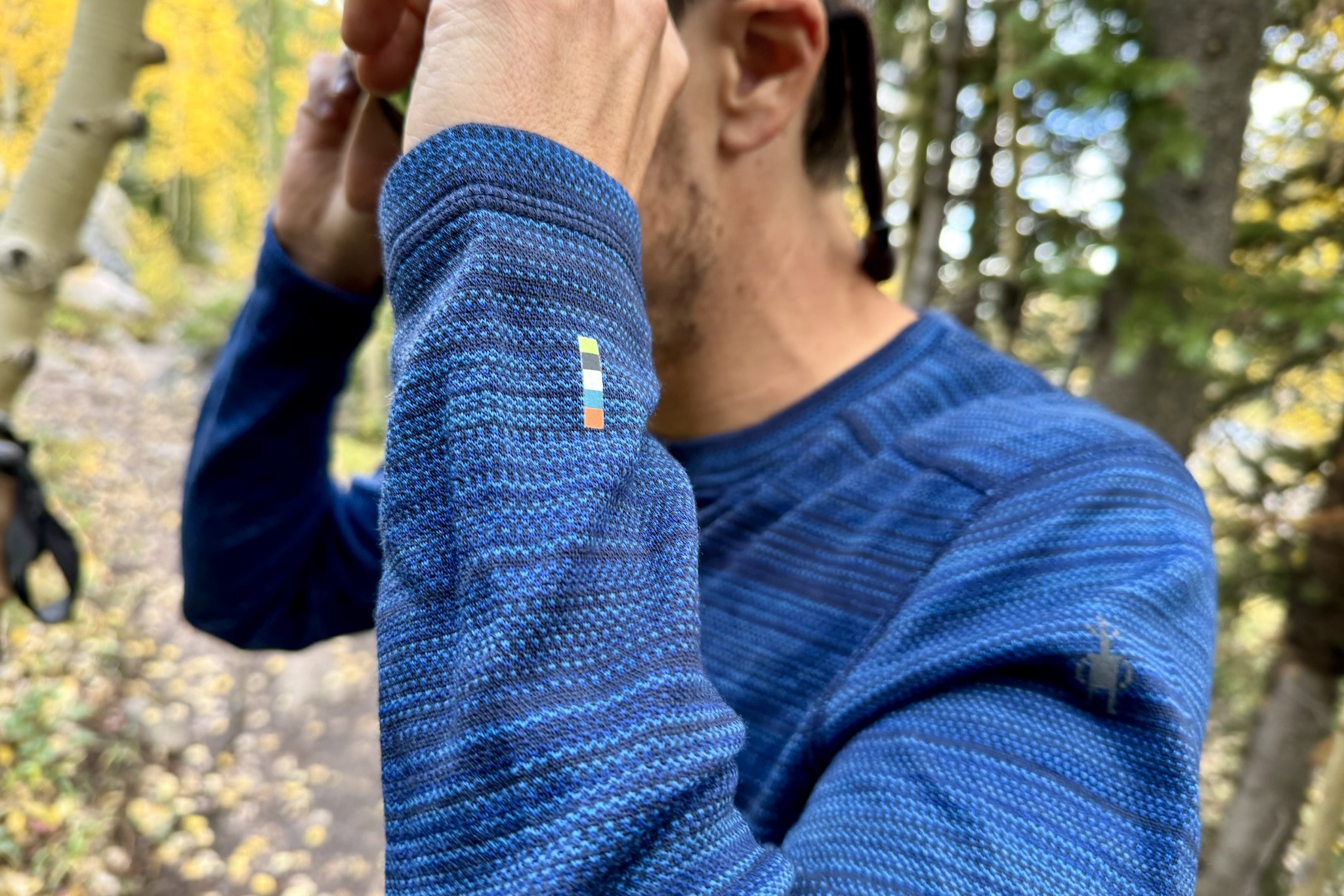 A hiker bends his arms, showing the wrist detail of the Smartwool Classic Thermal base layer. Trees are in the background.