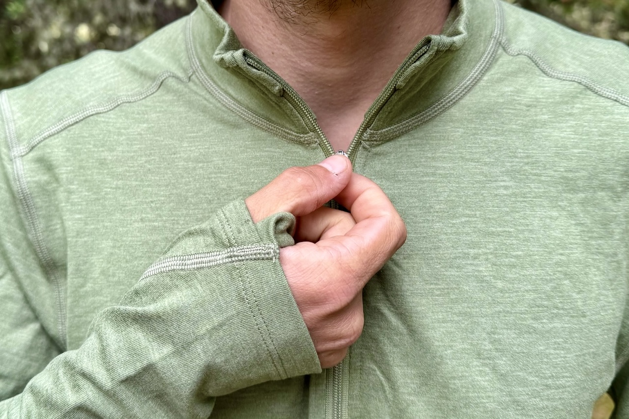 A close up of a hiker zipping up the zipper on the REI Midweight Half Zip base layer.