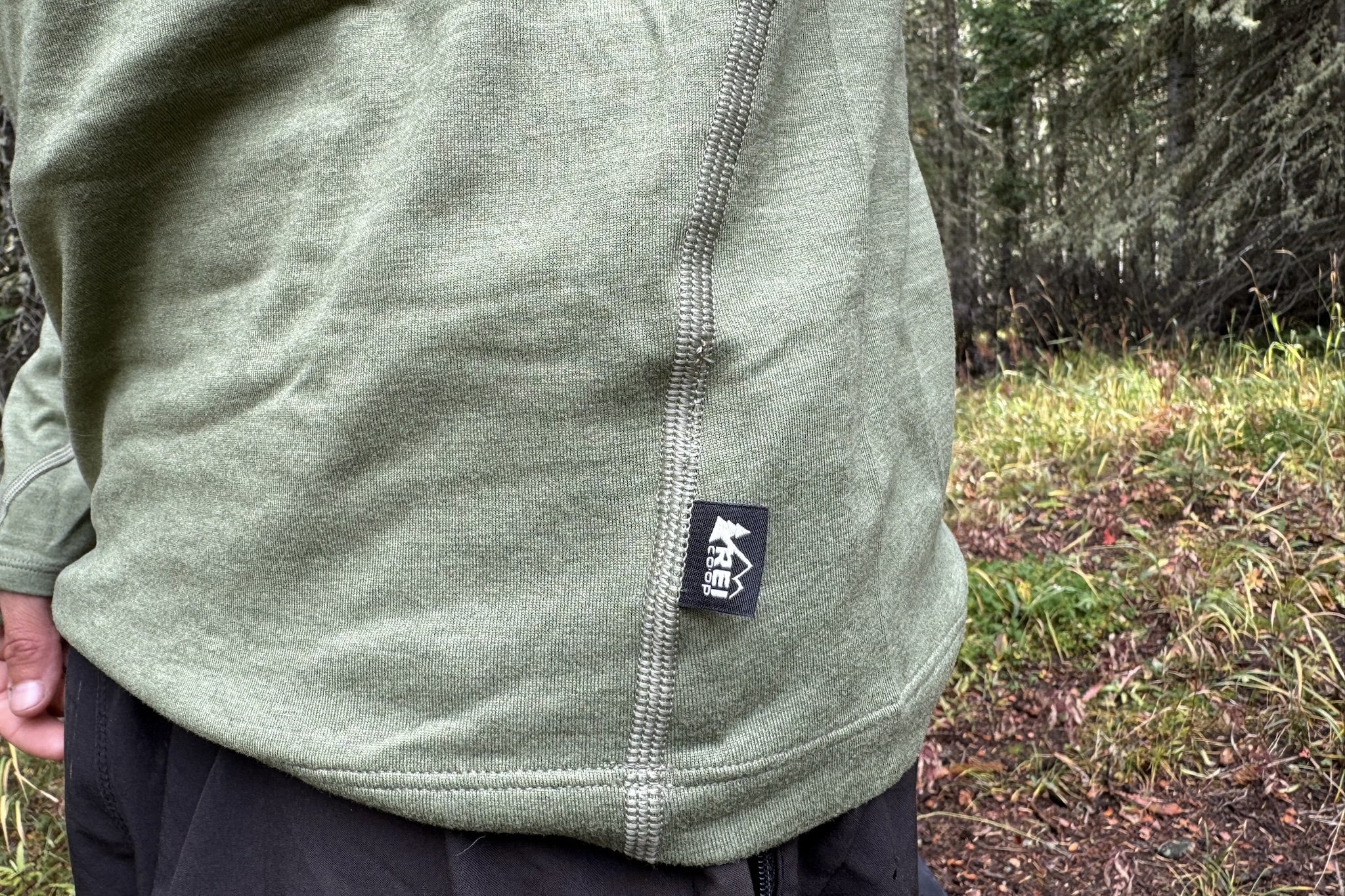 A closeup of the REI tag on the REI Midweight Half Zip base layer. Trees are in the background.