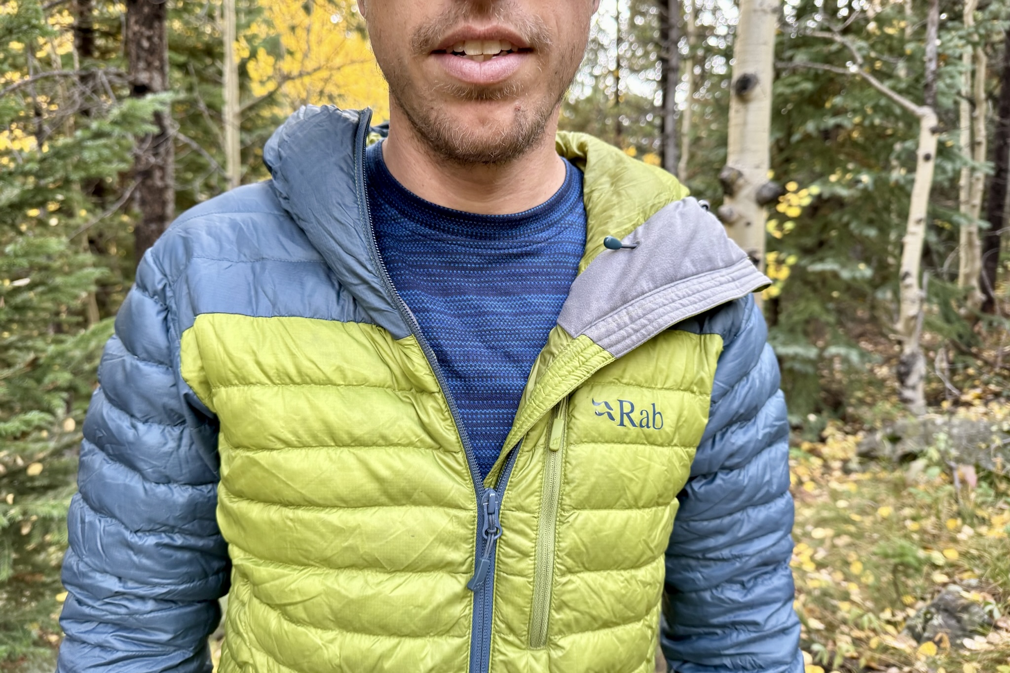 A hiker stands wearing the Smartwool Classic Thermal with a puffy jacket layered over top. Trees are in the background.