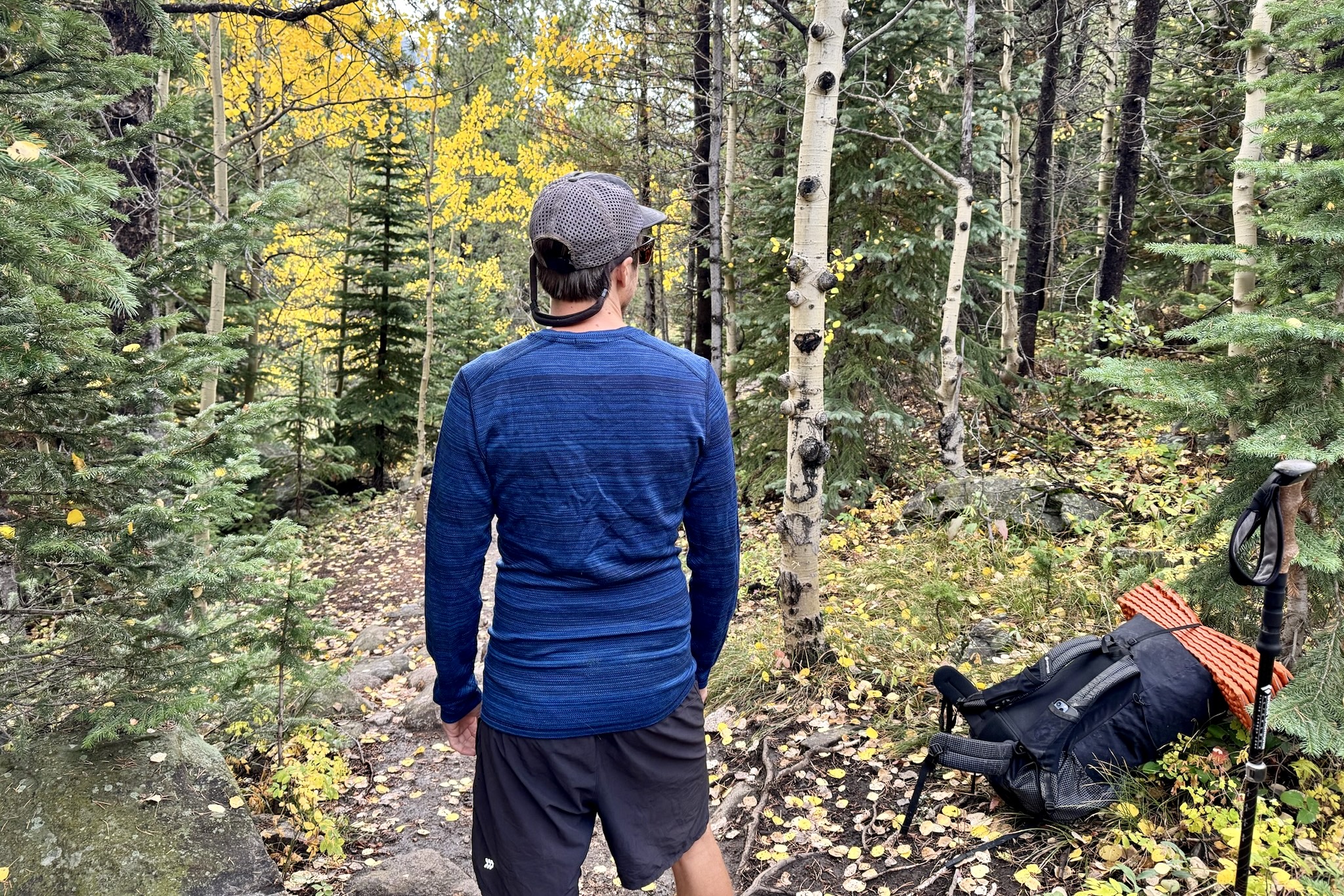 A hiker faces away from the camera wearing the Smartwool Classic Thermal base layer. A pack and trees are in the background.