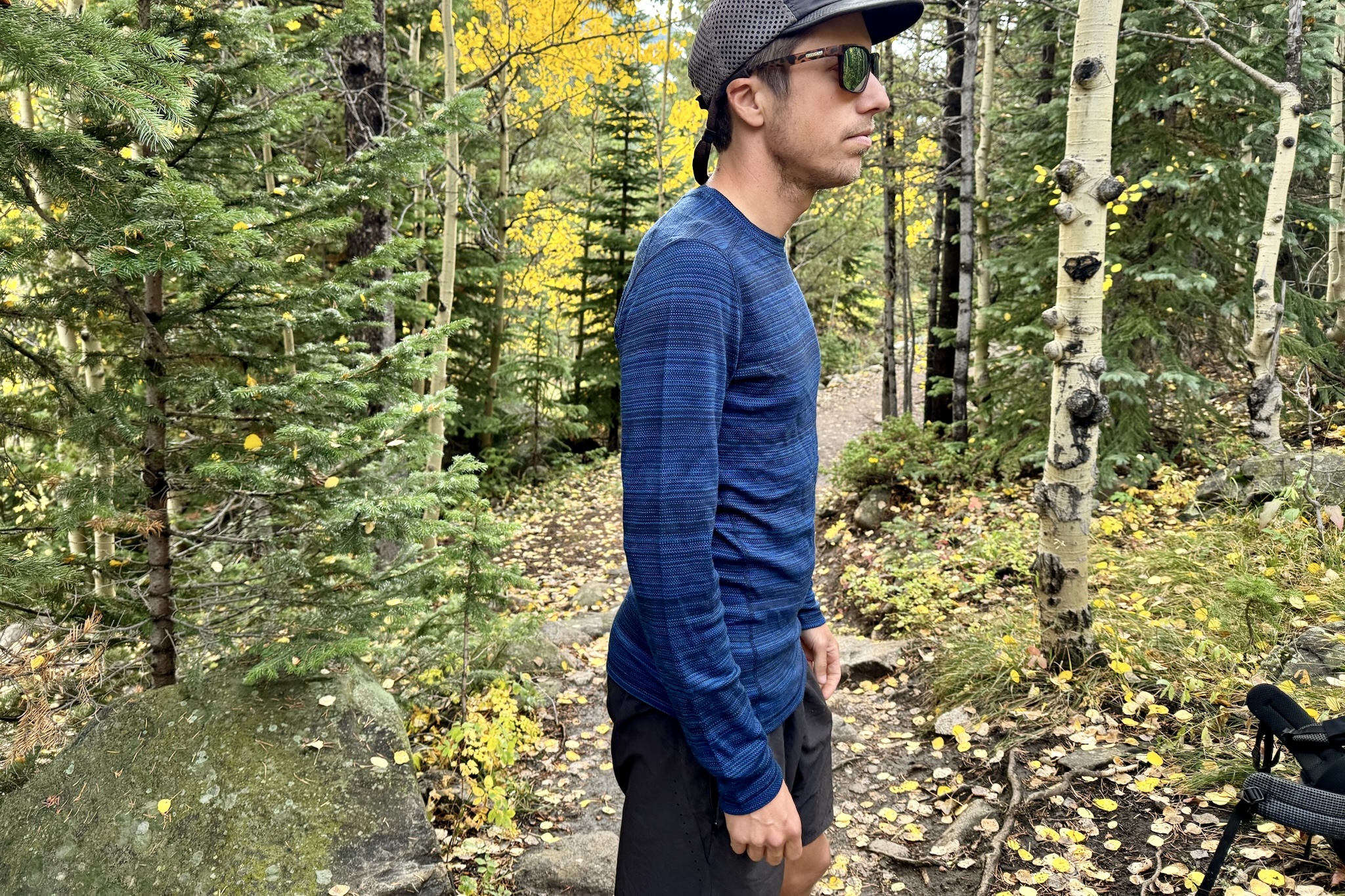 A hiker stands in the woods wearing theSmartwool Classic Thermal base layer. Trees and a trail are in the background.