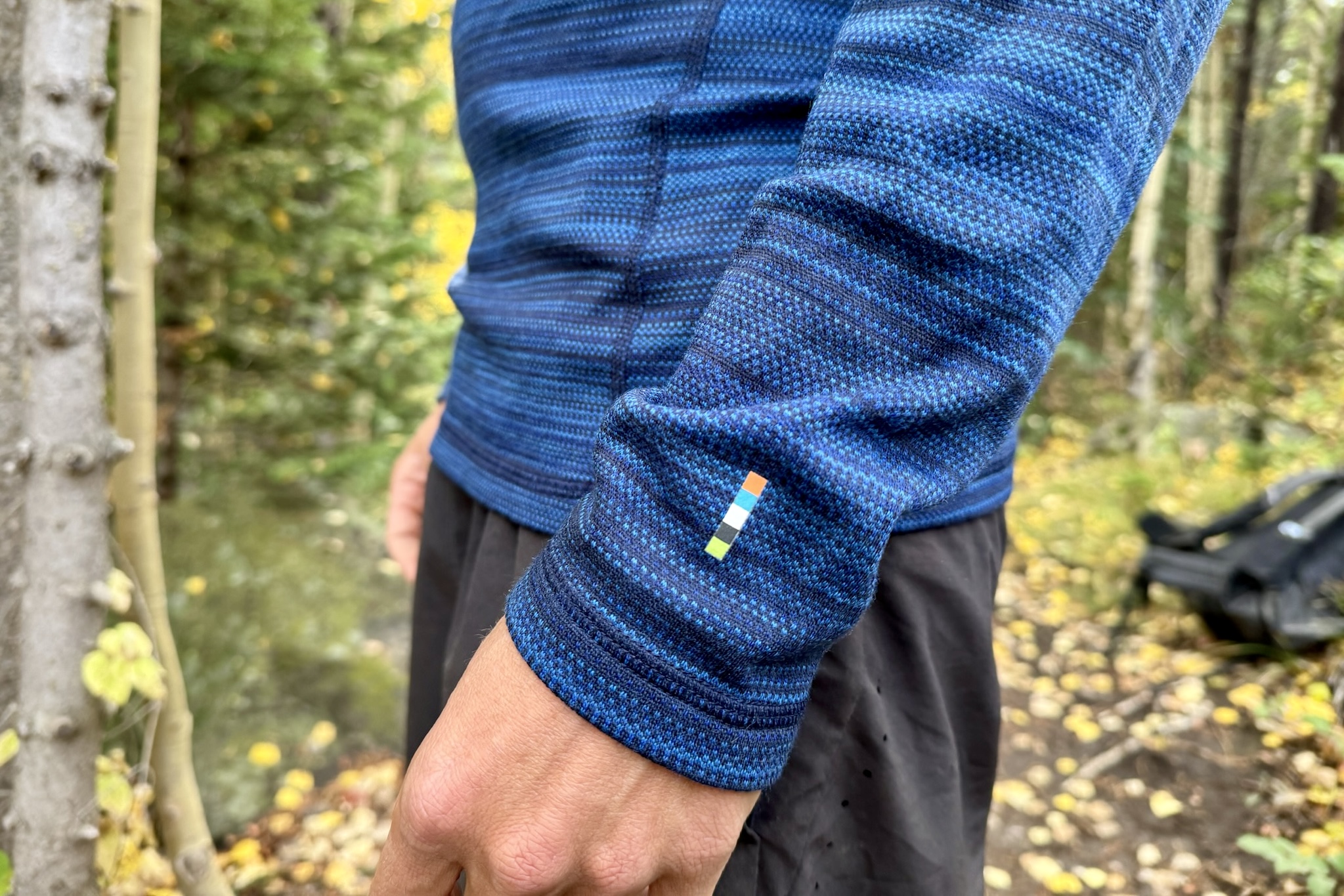 A close up of the wrist logo on the Smartwool Classic Thermal base layer. Trees and a backpack are in the background.