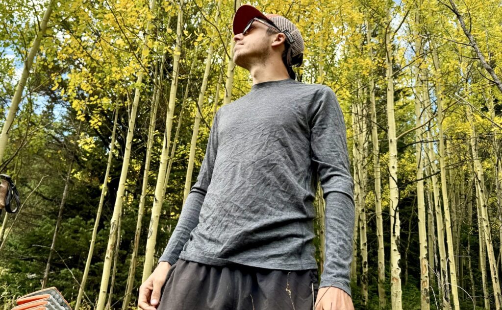 A hiker stands in the woods wearing the Smartwool Classic All-Season base layer. Trees are in the background.