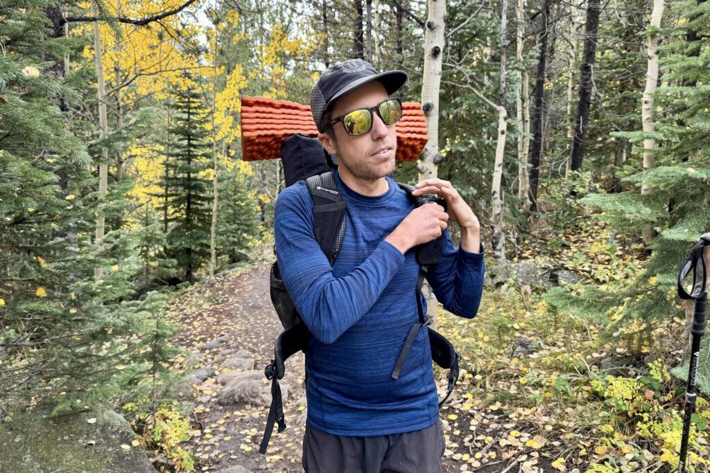 A hiker shoulders his pack while wearing the Smartwool Classic Thermal base layer. Trees are in the background.