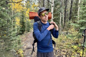 A hiker shoulders his pack while wearing the Smartwool Classic Thermal base layer. Trees are in the background.