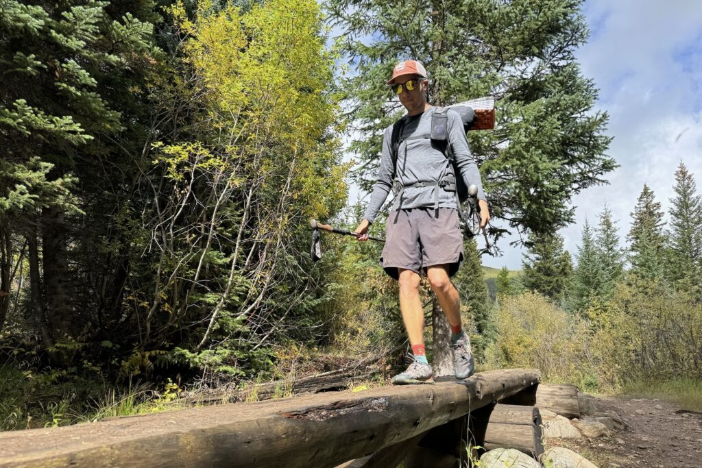 A hiker crosses a log wearing the Smartwool Classic All-Season base layer. Trees are in the background.