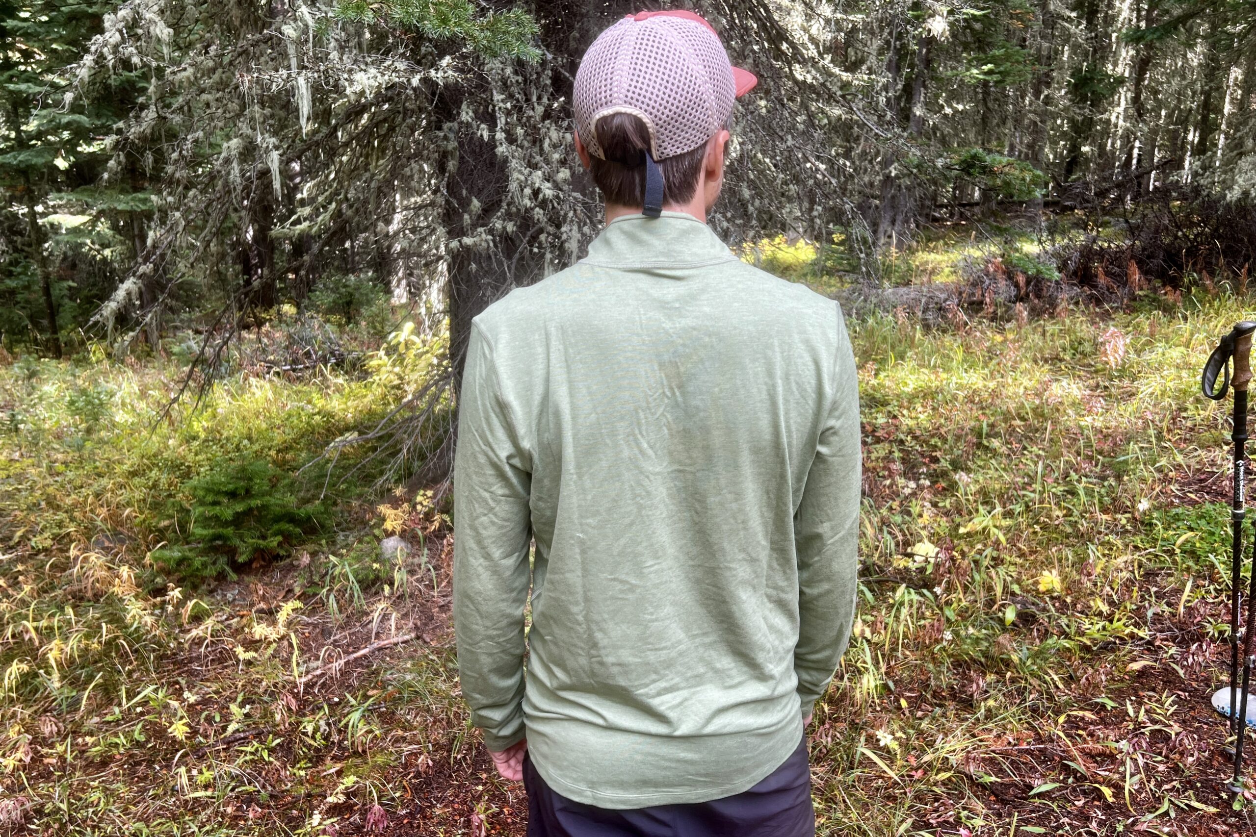 A hiker faces away from the camera while wearing the REI Midweight Half Zip base layer. Trees are in the background.