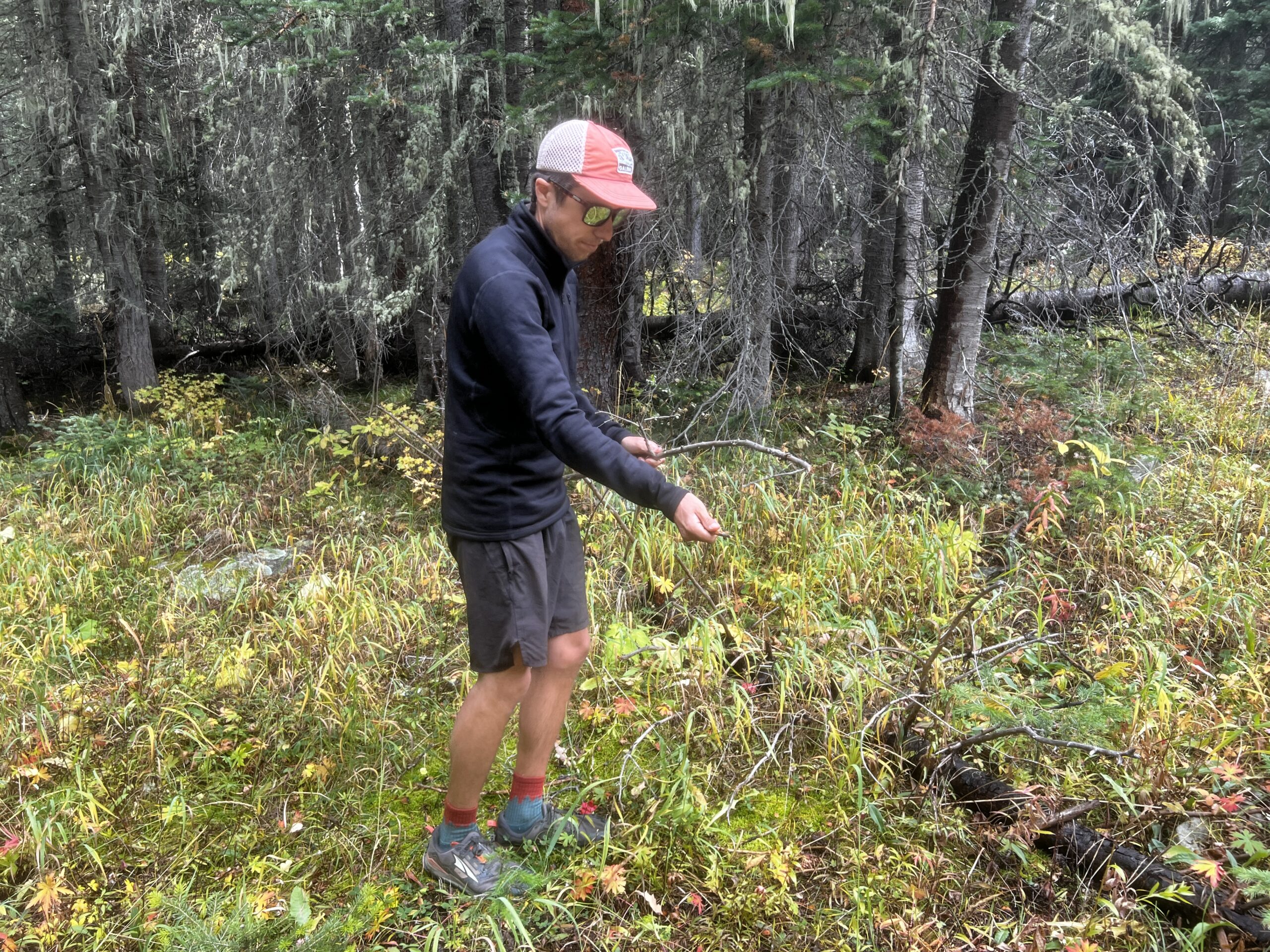 A hiker breaks up kindling while wearing the Arc'teryx Rho Heavyweight Zip Neck base layer. Trees are in the background.