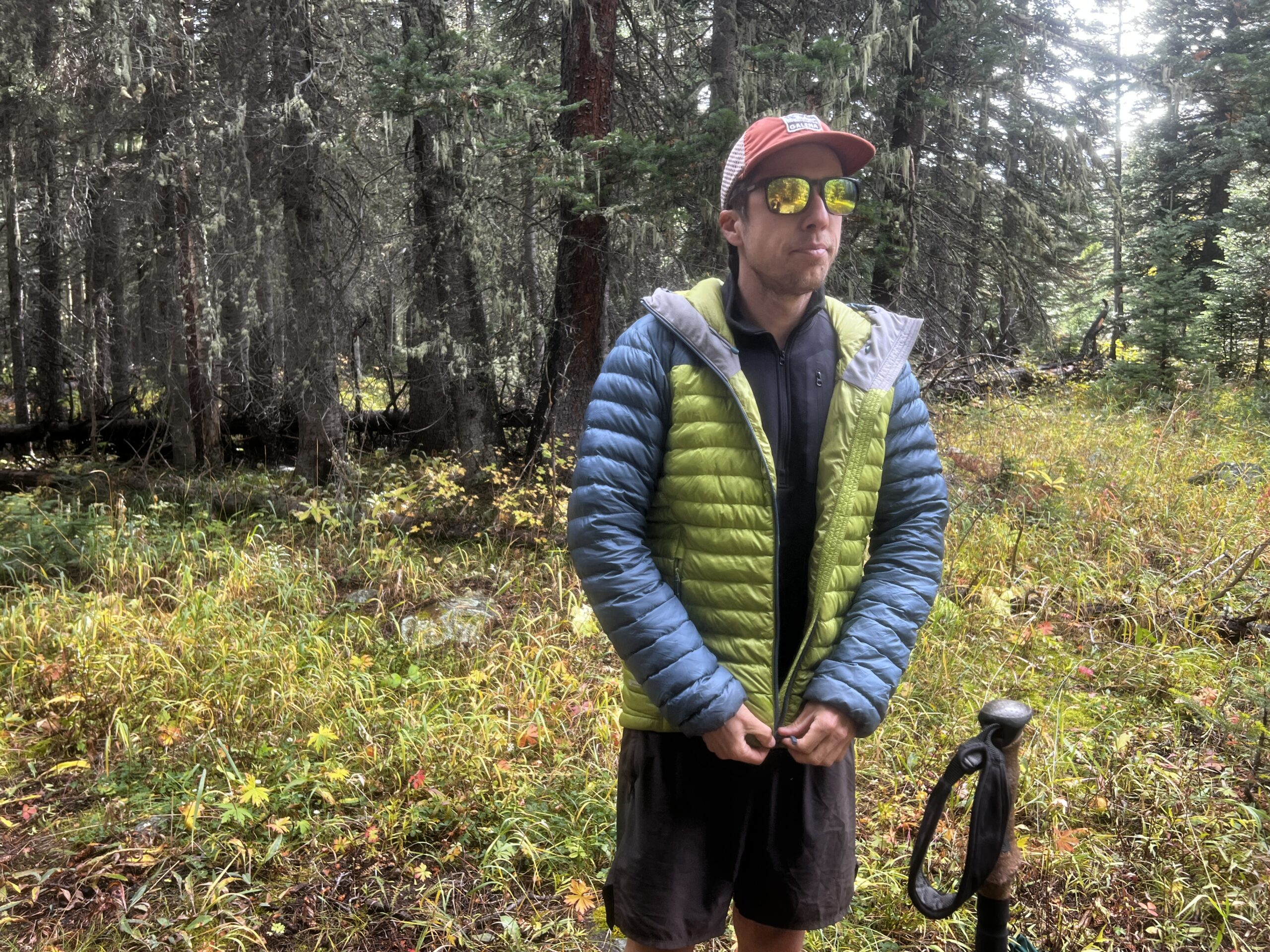 A hiker zips up a jacket over top of the Arc'teryx Rho Heavyweight Zip Neck base layer. Trees are in the background.