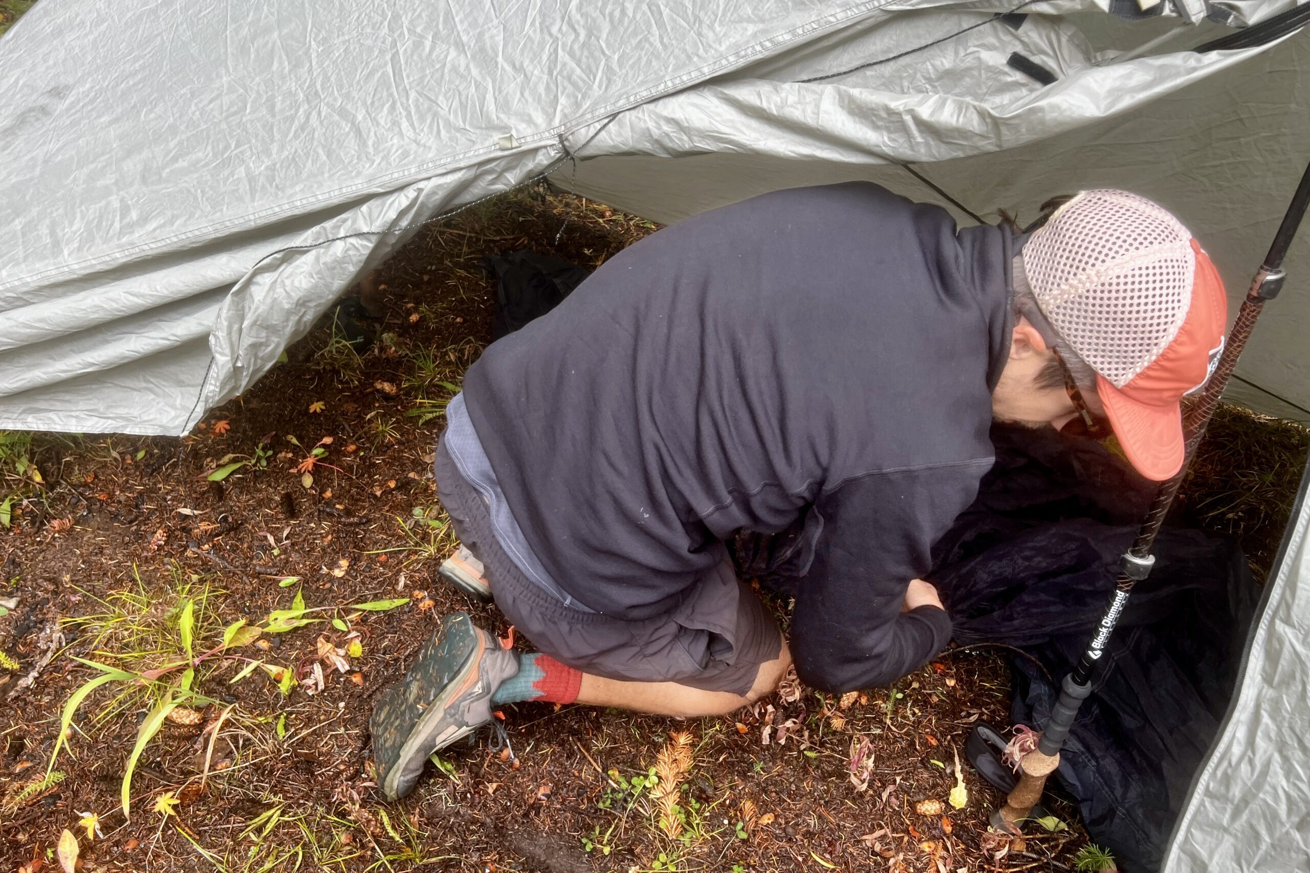 A hiker sets up his tent while wearing the Arc'teryx Rho Heavyweight Zip Neck base layer. A tent is in the background.