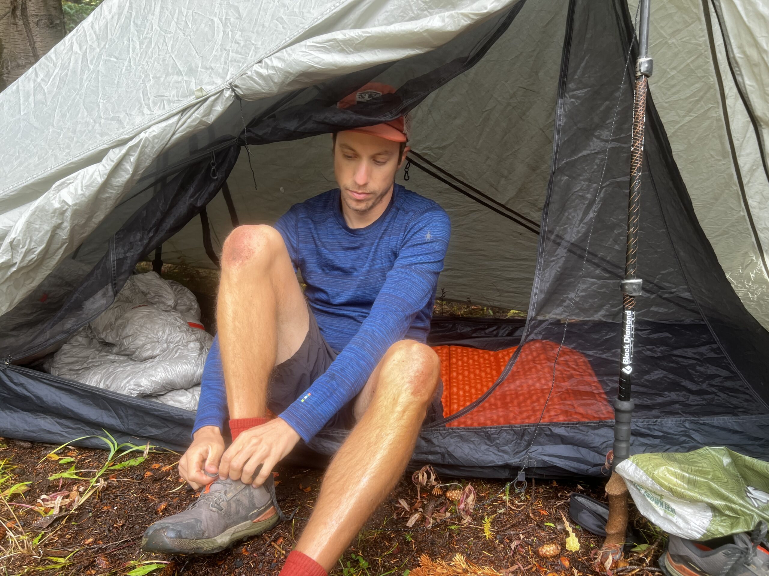 A hiker sits in his tent and puts on his shoes while wearing the Smartwool Classic Thermal base layer.