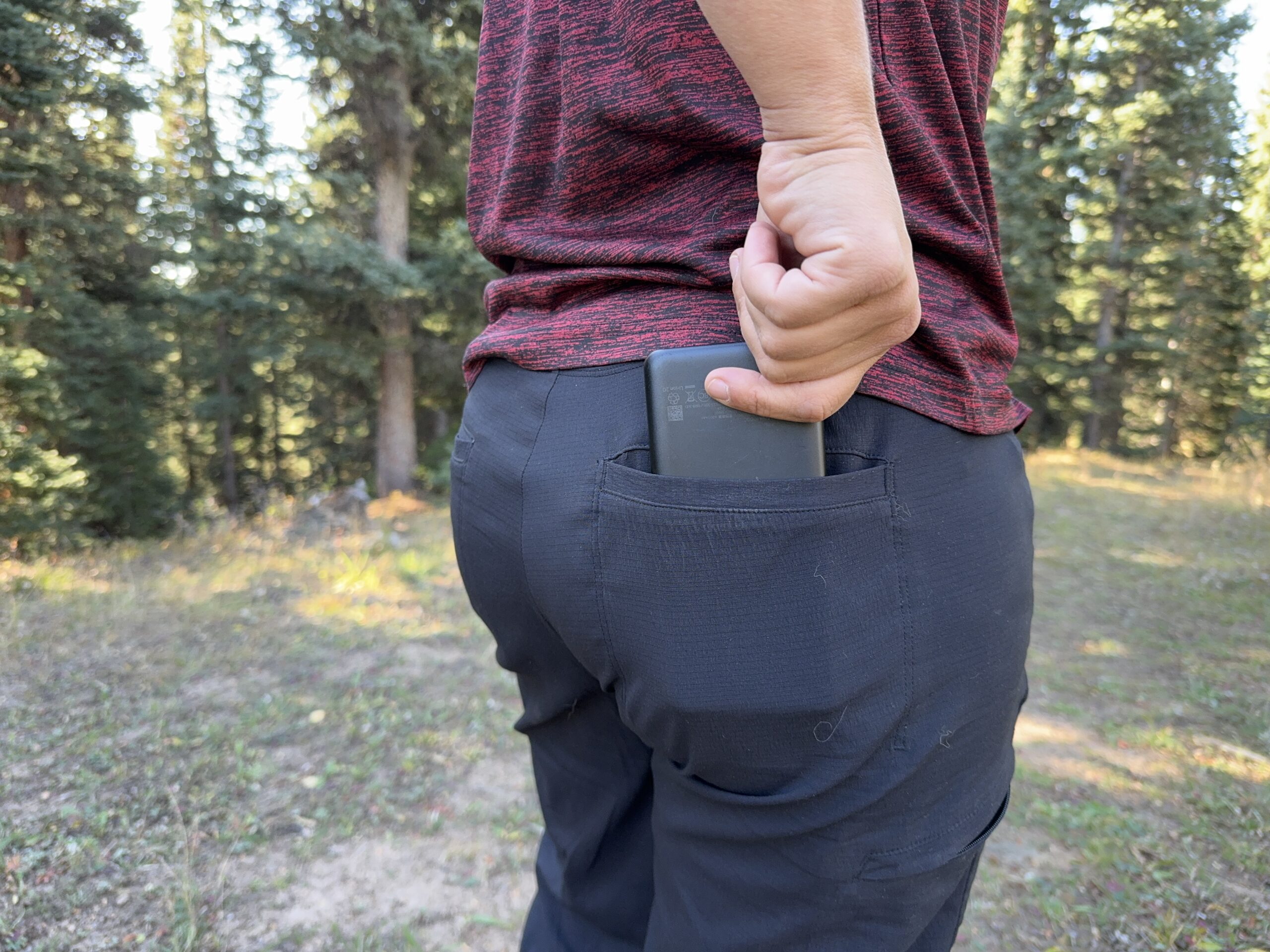 A person's hand placing a power bank into the back pocket of the Athleta Trekkie pants.