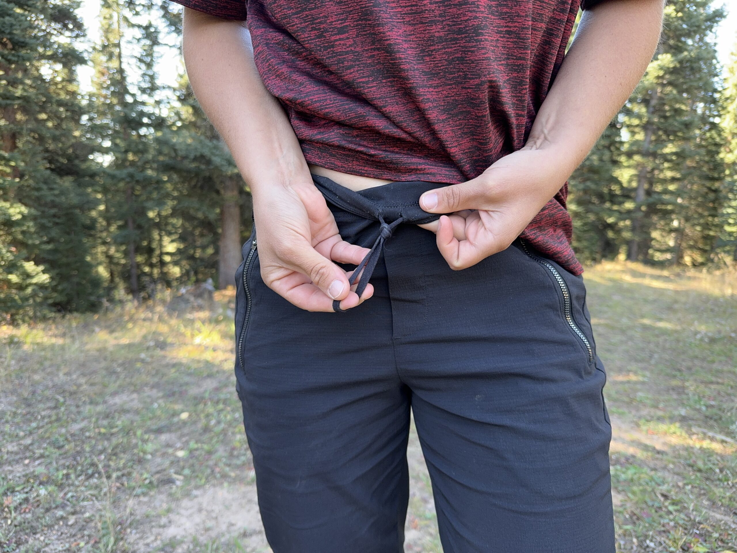 A person demonstrating that the Athleta Trekkie pants have an elastic drawstring in the waist.