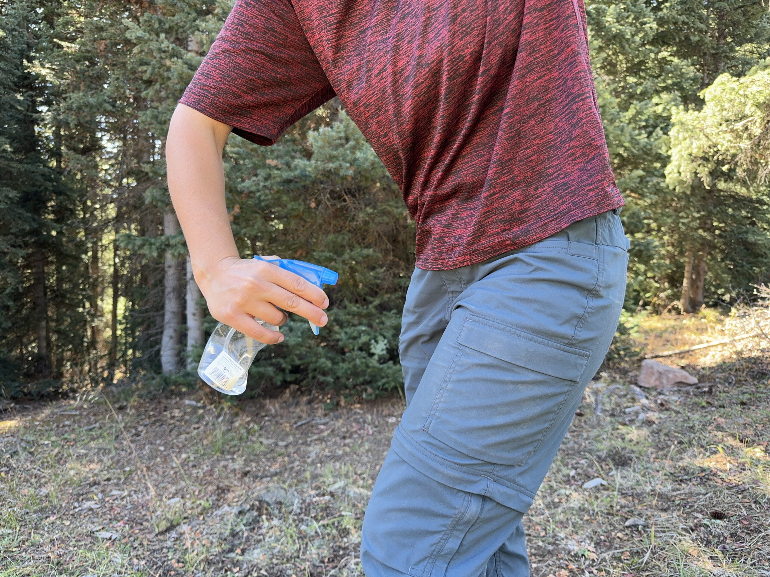 A person is using a squirt bottle to spray the REI Sahara pants with water.