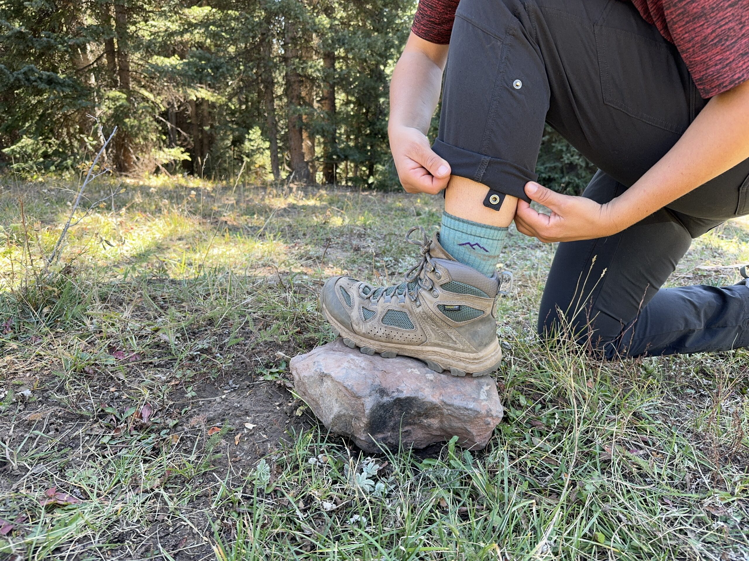 a hiker with their foot on a rock rolling up the ankle cuff of their kuhl freeflex pants