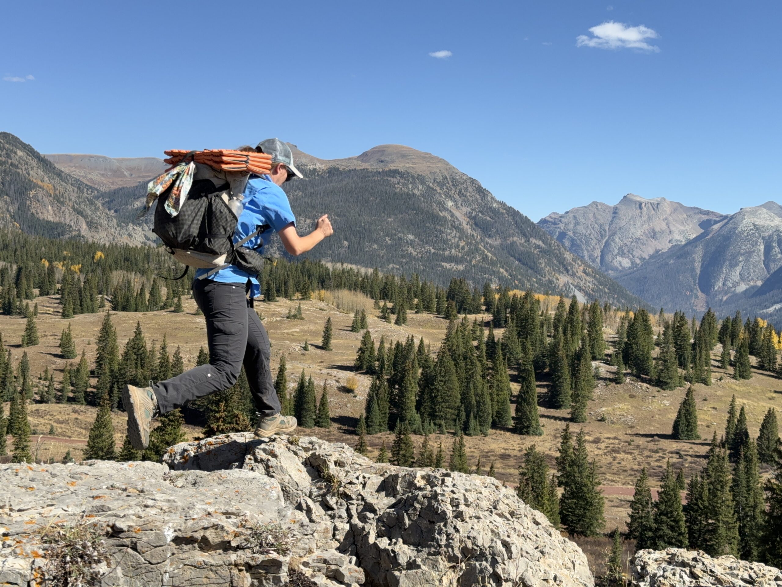 a hiker stepping across some rocks with blue skies and mountains in the distance