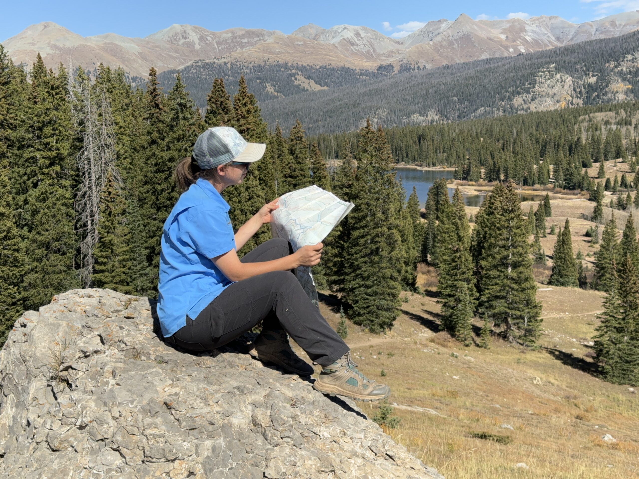 a hiker reading a map while seated on a rock in the mountains wearing the Kuhl freeflex rollup pant