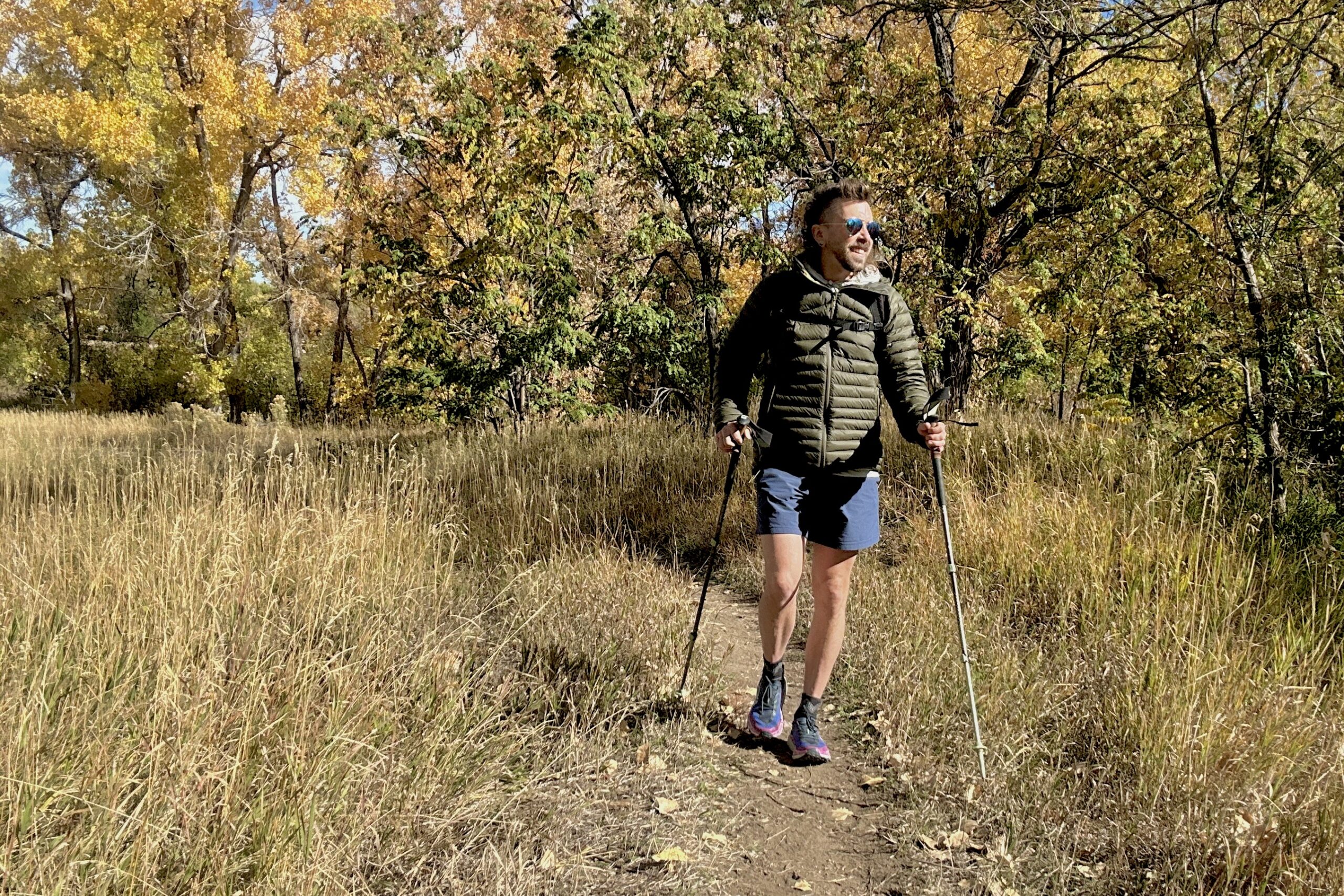 A man hikes through a forest in fall colors smiling.