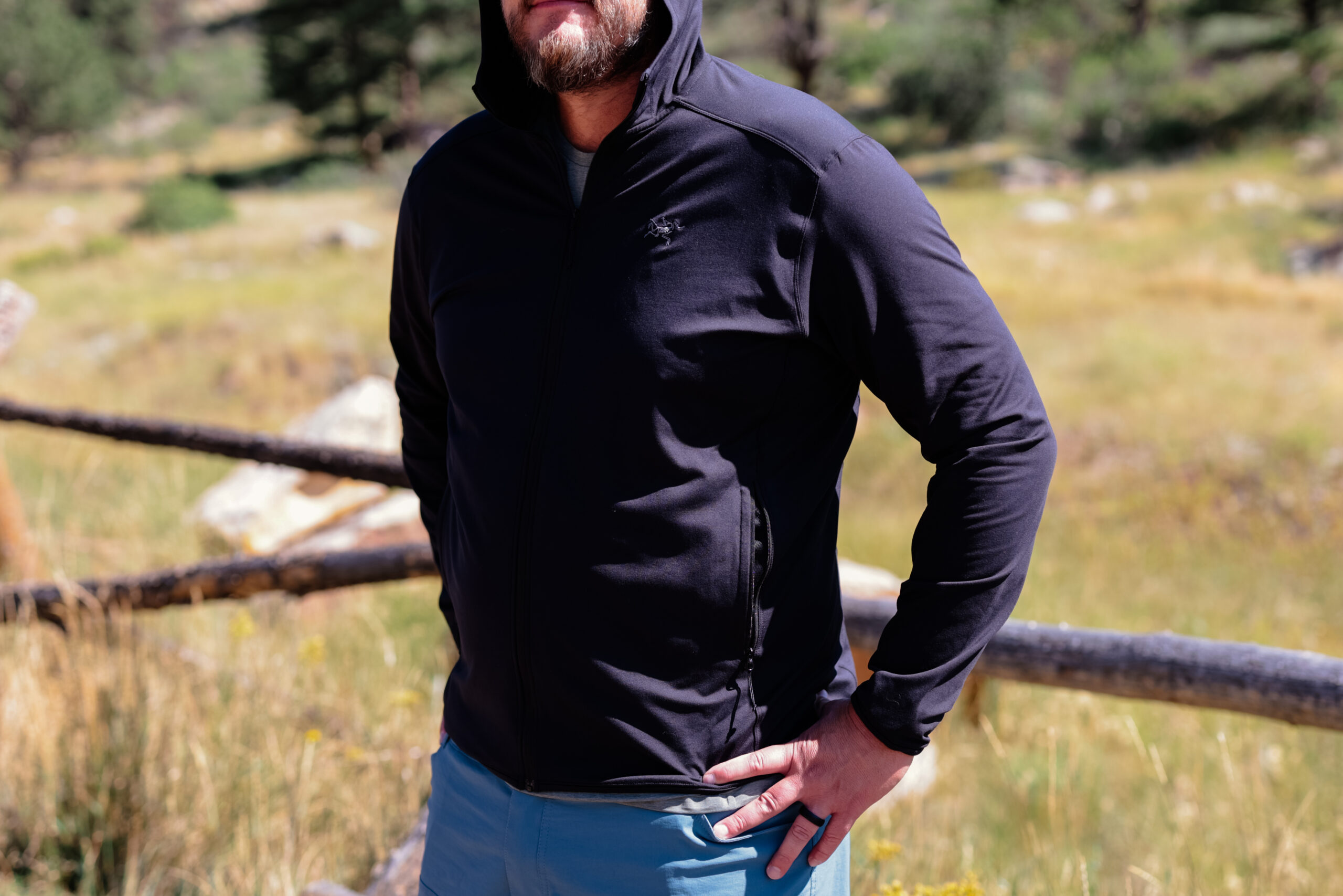 Man standing by a wooden fence with hands on hips.