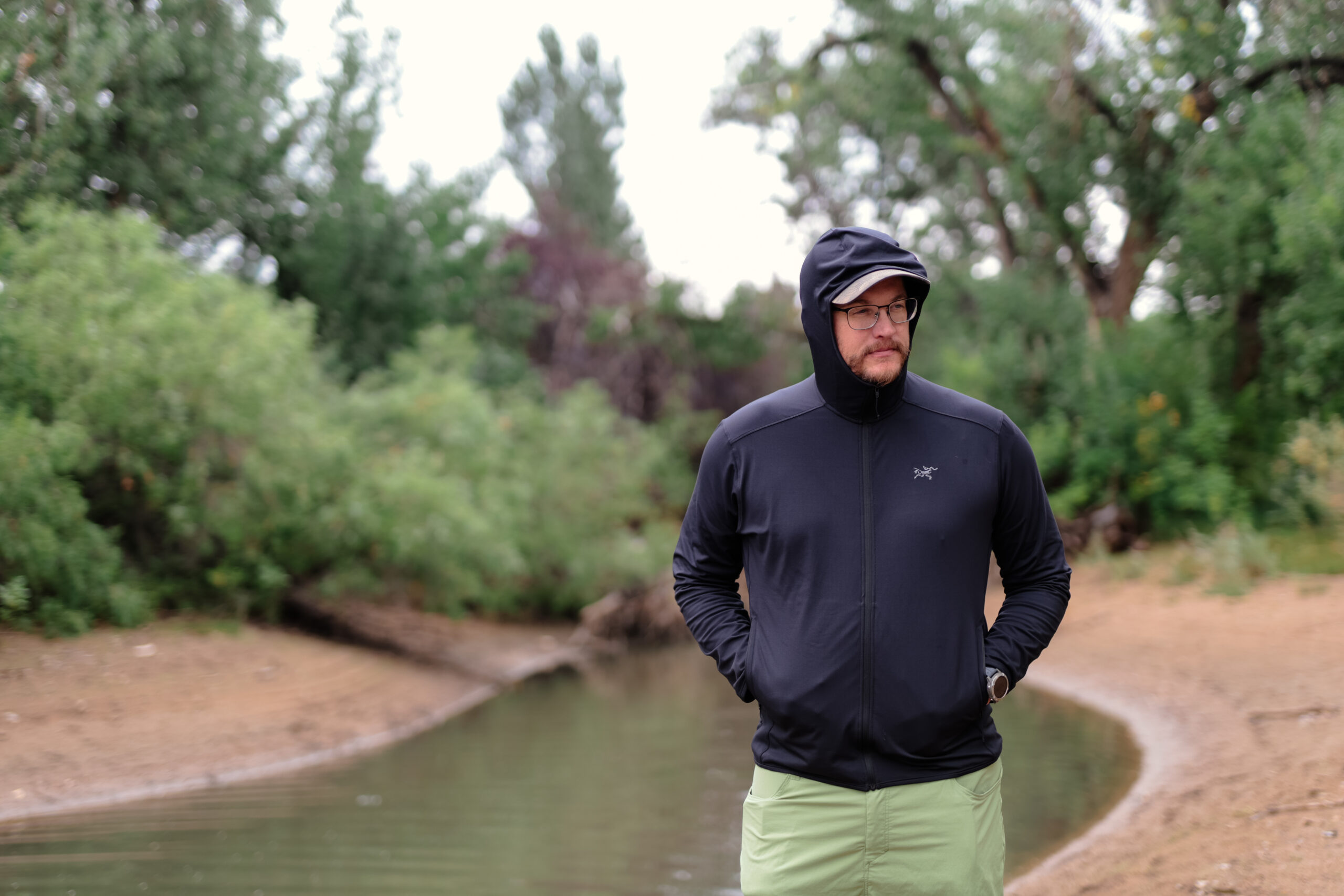 Man walks by a river with a fleece hood up.