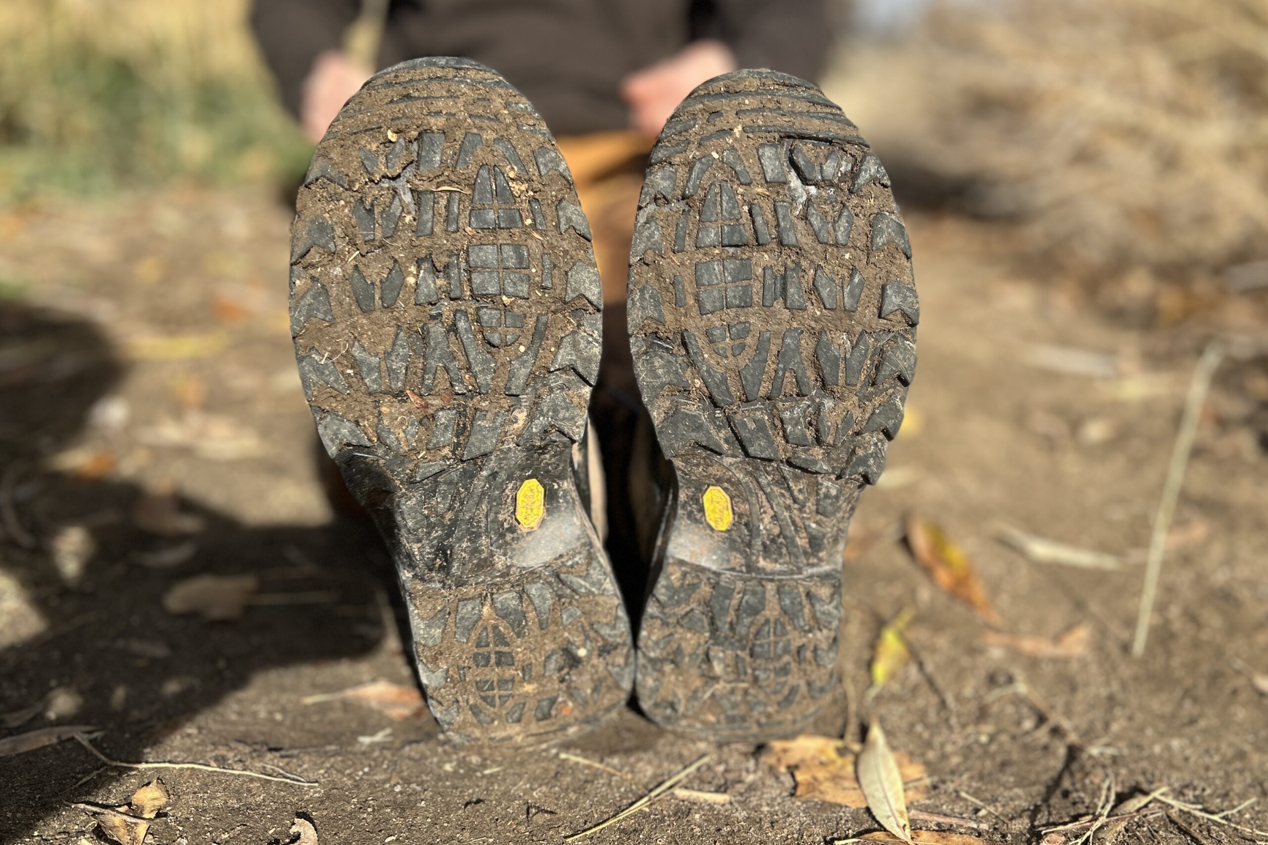 The bottom of a pair of hiking boots showing off both the tread pattern and all the mud stuck in it.