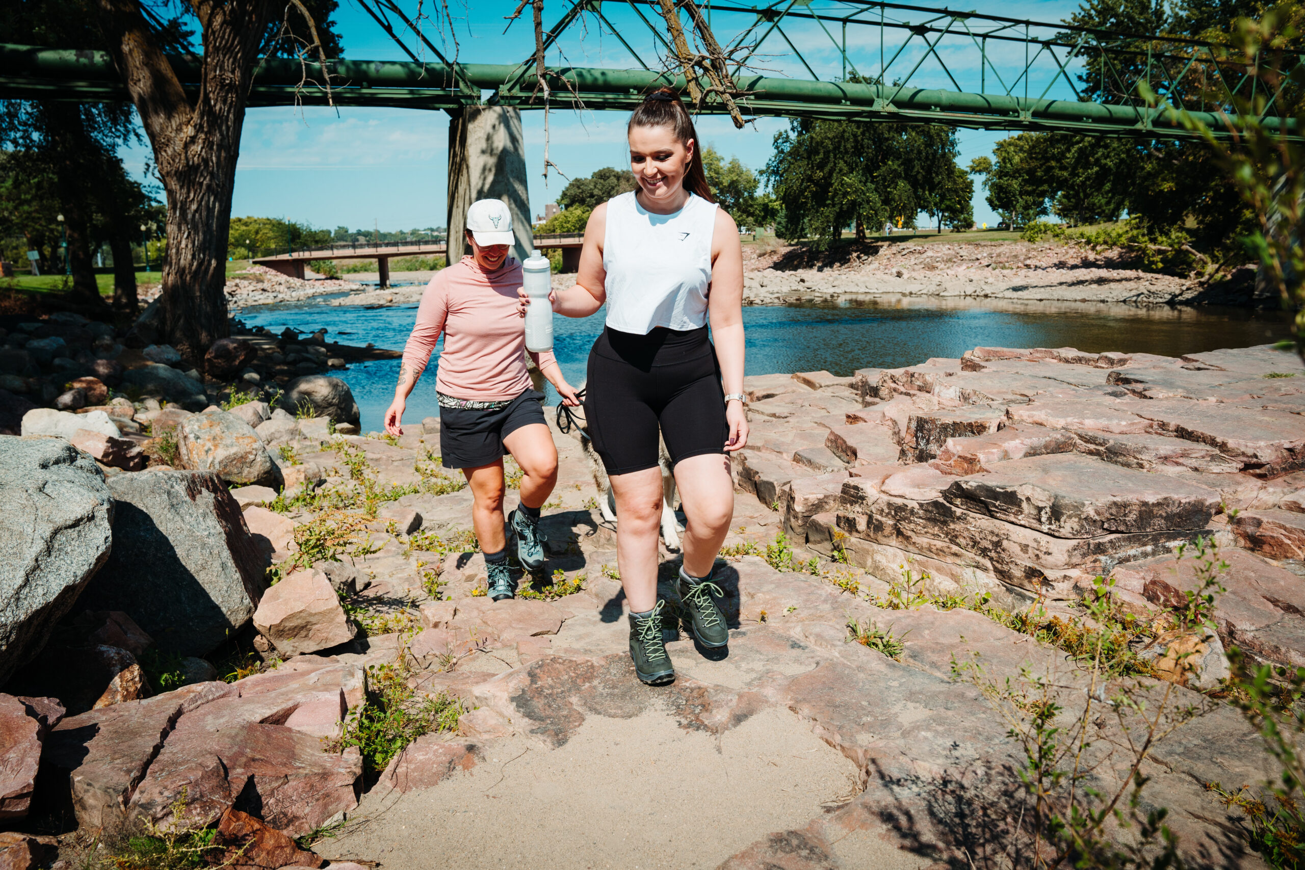 Two female hikers crossing over a rocky path overlooking a river