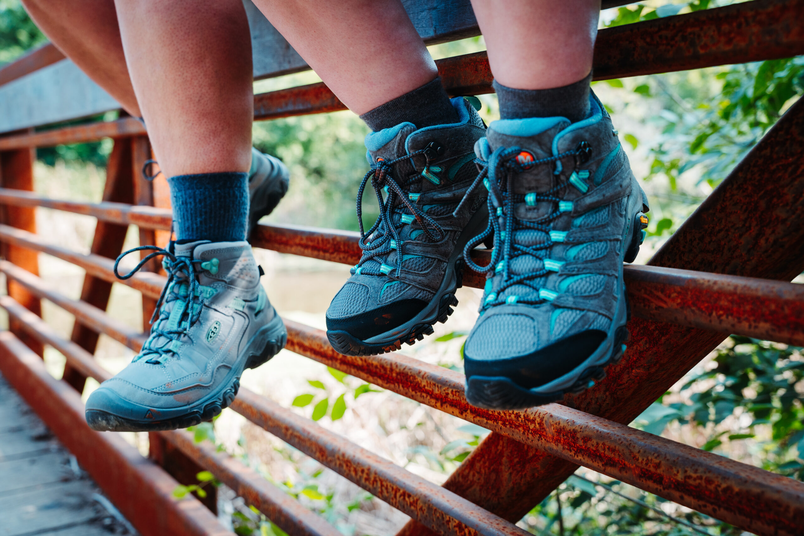 Two hikers sitting on a bridge wearing Women’s KEEN Targhee IV WP and Women’s Merrell Moab 3 WP hiking boots