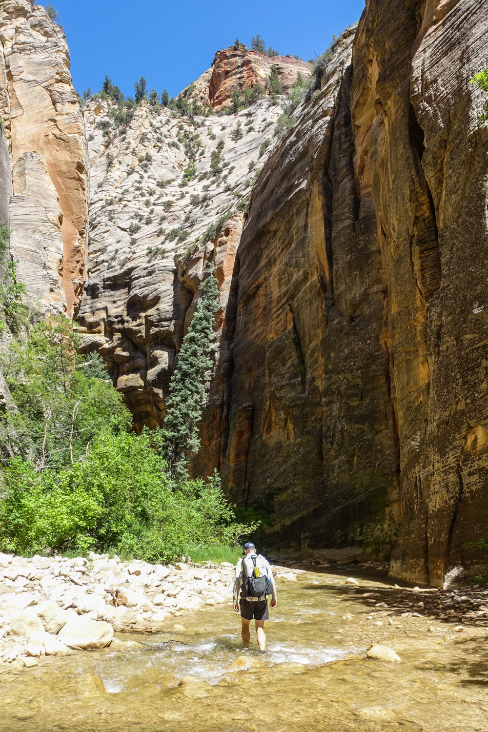 a backpacker walks in the shallow river heading into a canyon