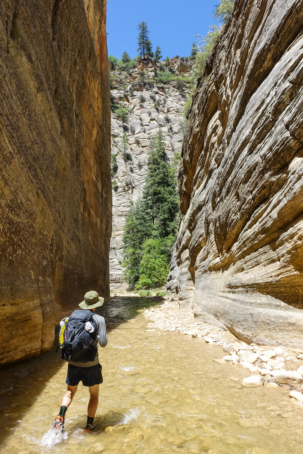 a hiker walking into a slot canyon in shallow river water