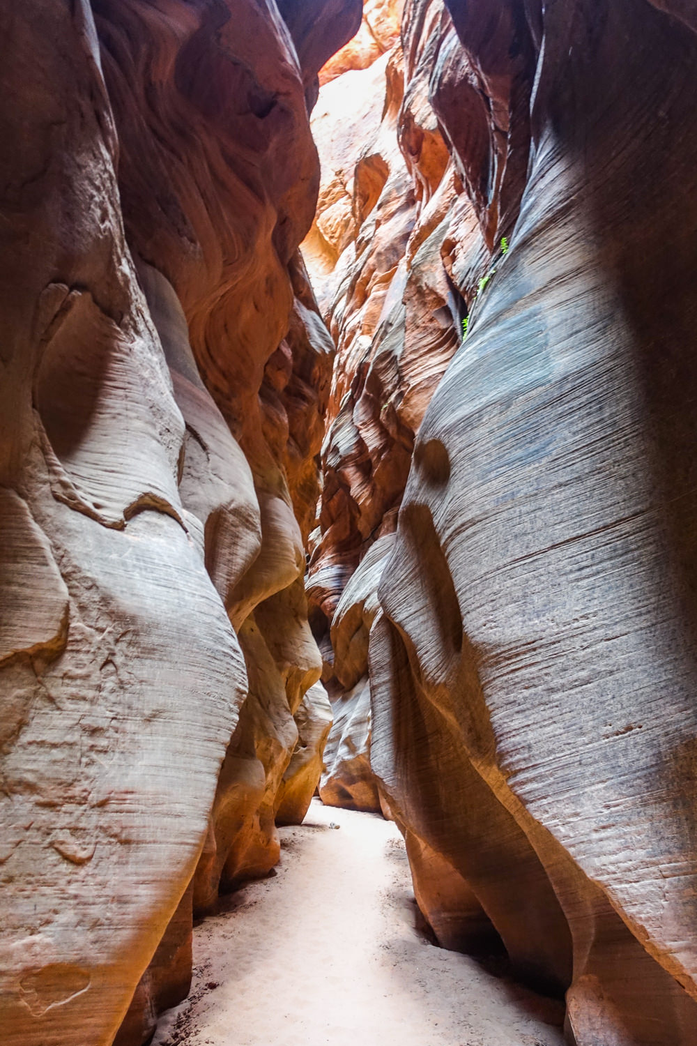 the sandy and narrow path through a slot canyon with red and orange sandstone cliffs on both sides