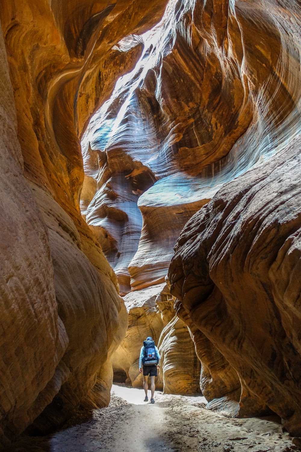 a backpacker heads toward a sunlit section of a slot canyon