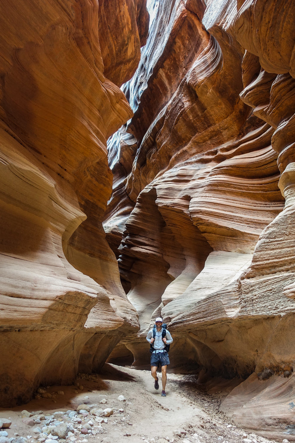 backpacker walking toward the camera through a narrow and wavy slot canyon in utah