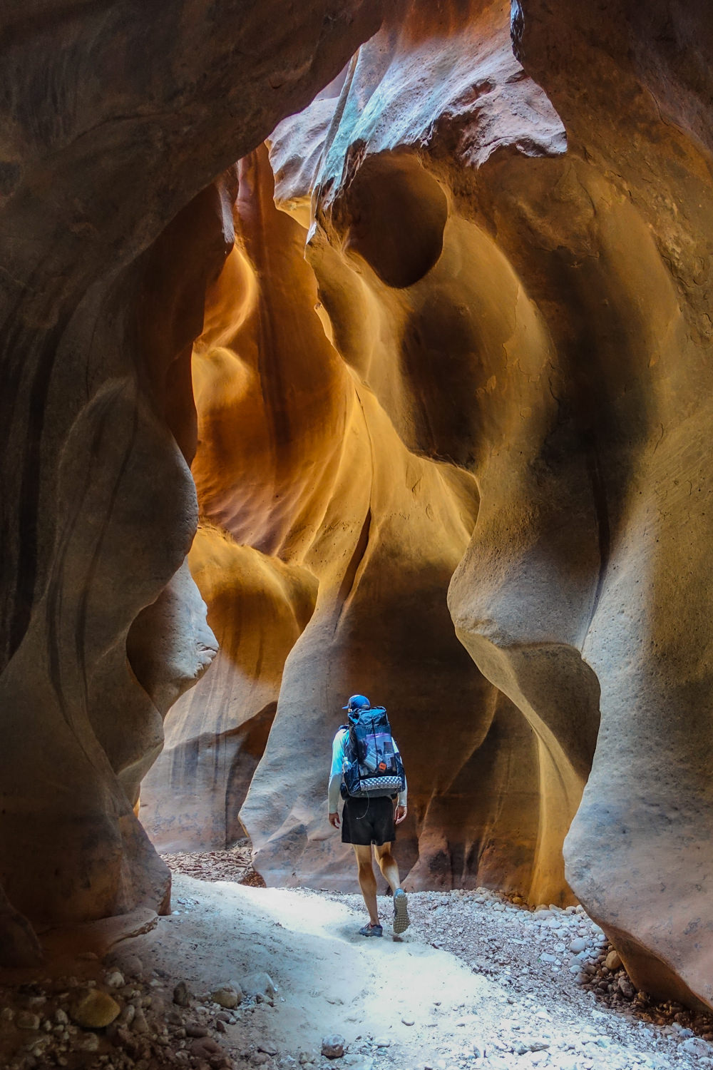 a hiker walking through a slot canyon in buckskin gulch with rounded walls of sandstone on both sides