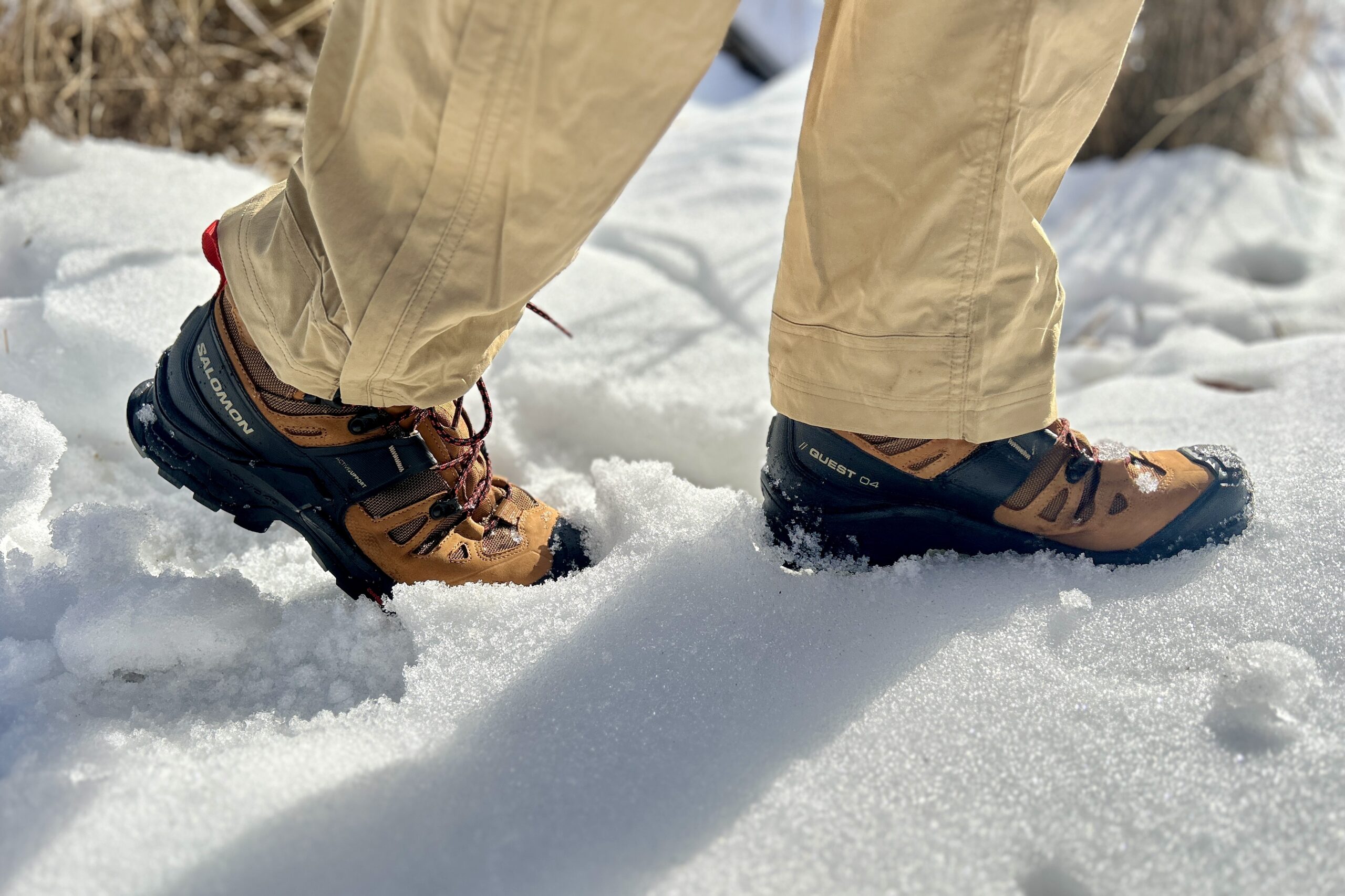 Close-up image from the knees down of a person walking in hiking boots in snow.