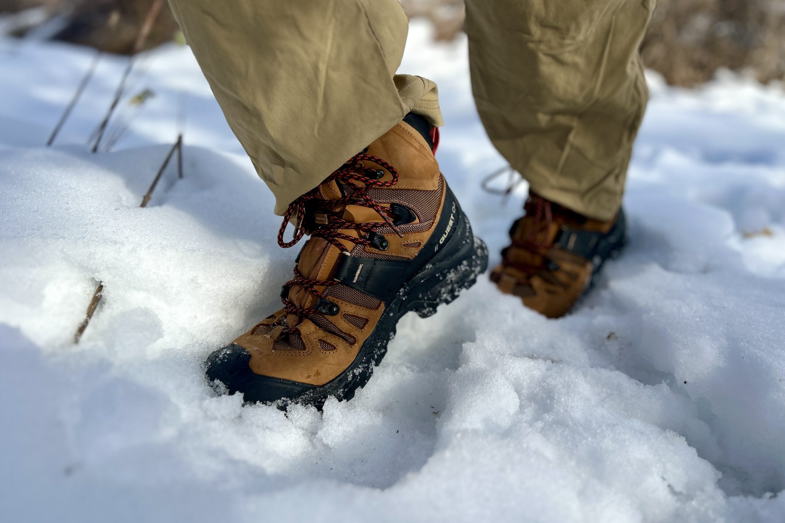 Close-up image from the knees down of a person walking in hiking boots in snow.