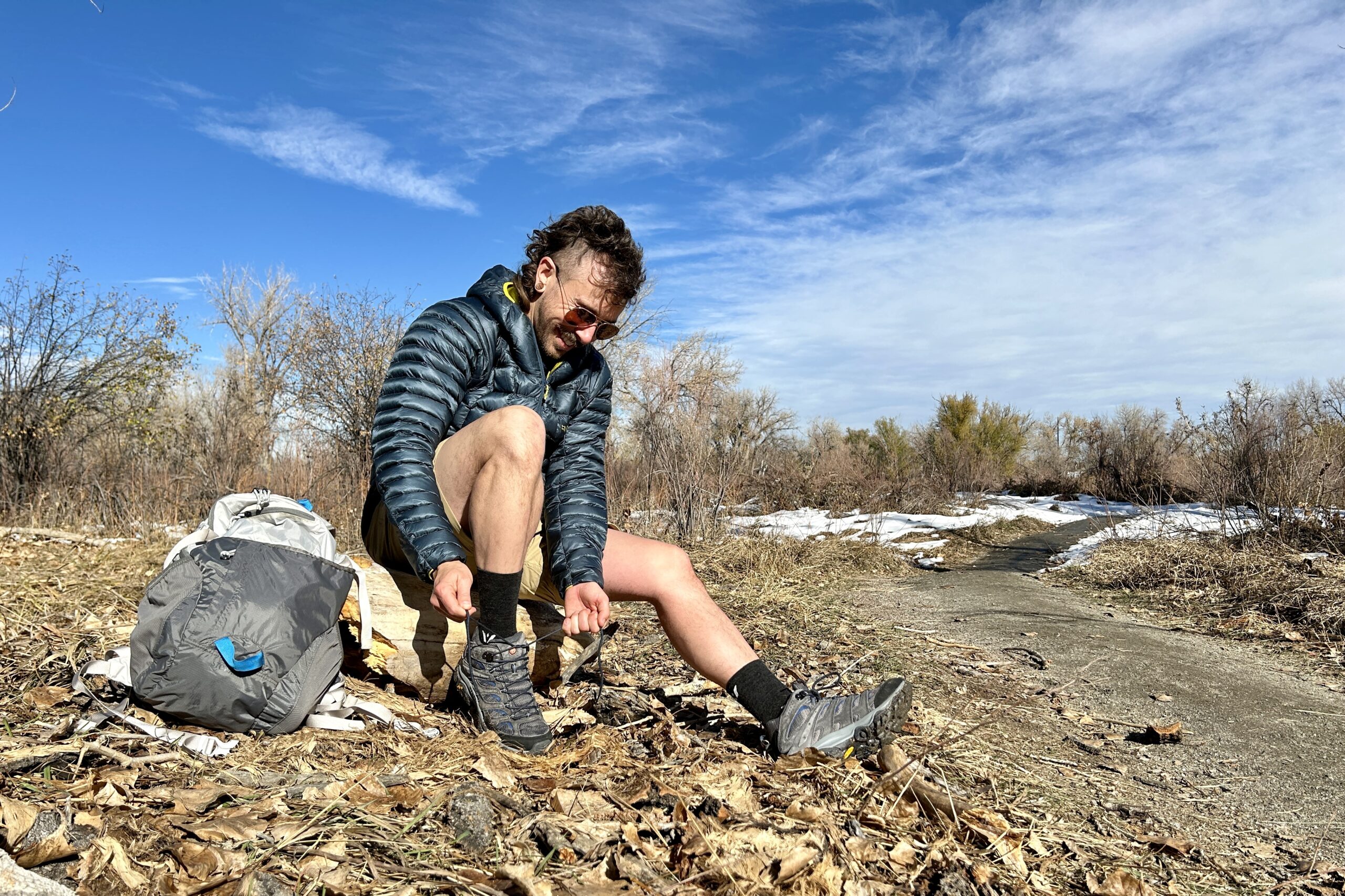 A man adjusts his hiking boots while sitting on a log in a wilderness area.