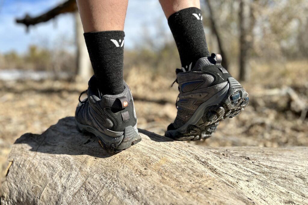 Close-up image from the knees down of a person walking in hiking boots in a wilderness area.