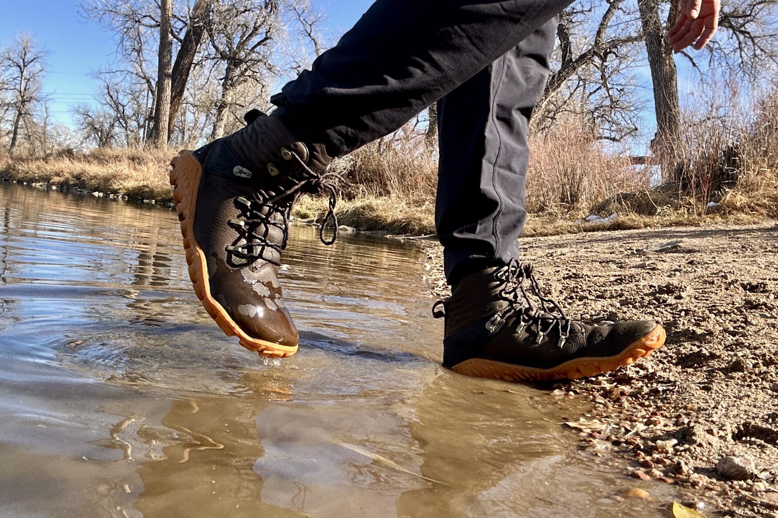 Close up image from knees down of a person walking through a creek.