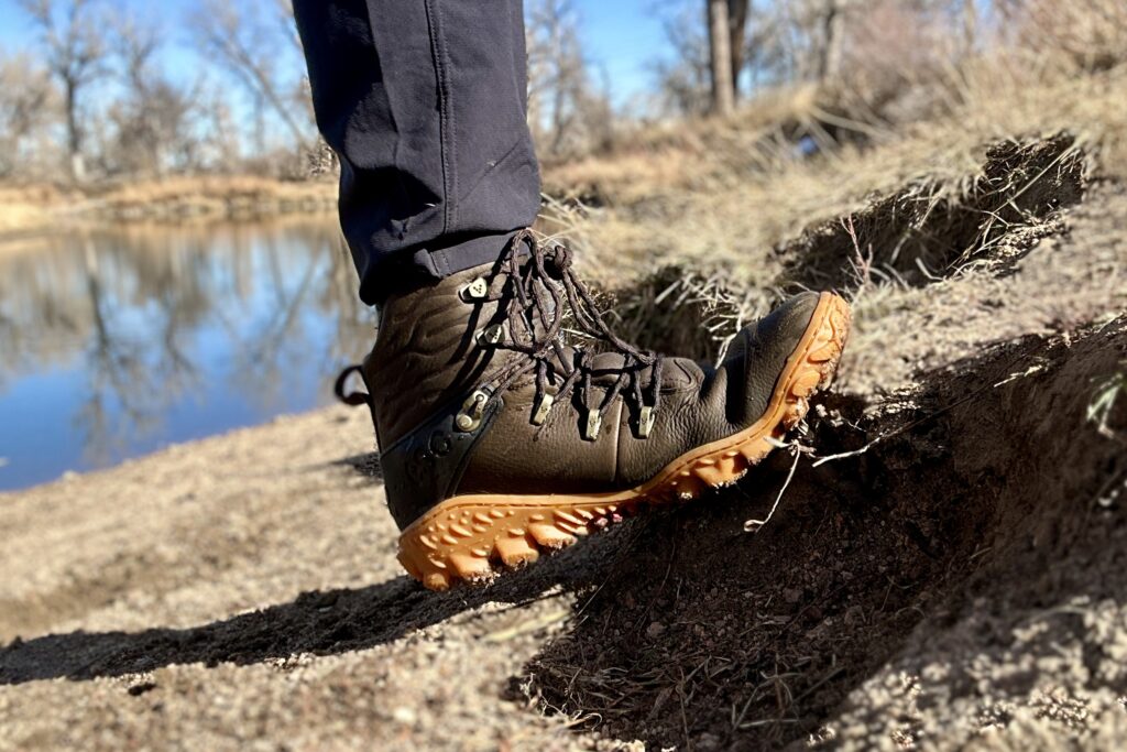 Close up image from knees down of a boot flexing against a slight incline near water.